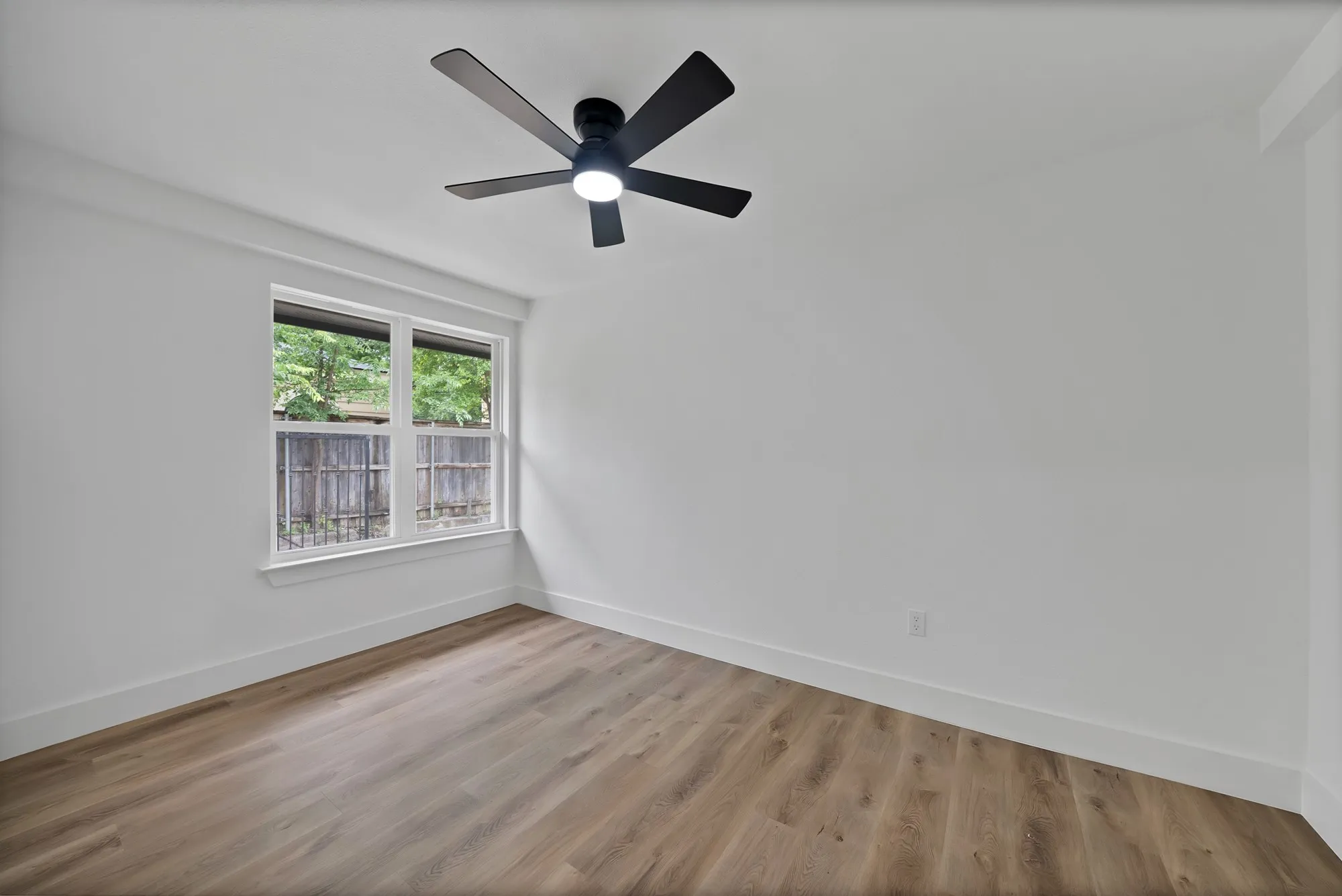 Spacious room featuring wood-finish flooring, a contemporary ceiling fan with integrated lighting, and a double window
