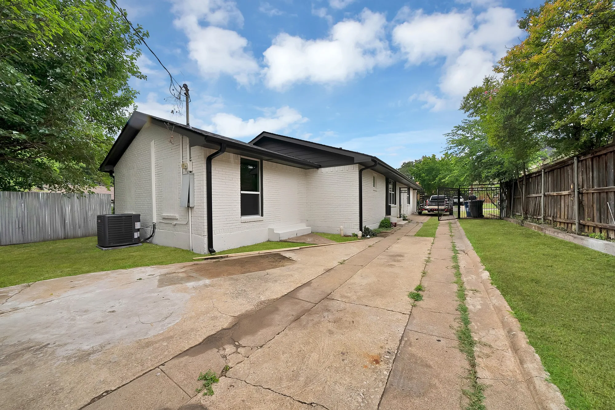White brick exterior with black trim, featuring a concrete driveway, a manicured lawn, and a privacy fence