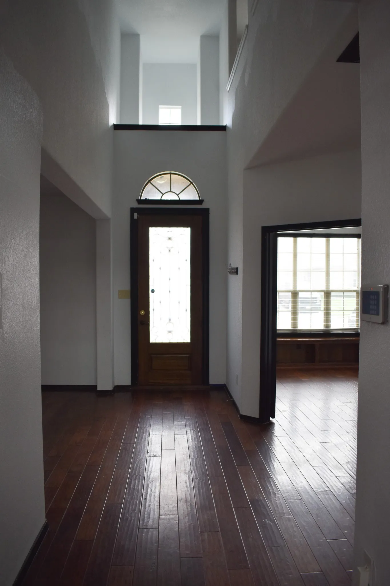 Two-story foyer featuring dark wood-finish flooring and a wood-paneled front door with decorative glass