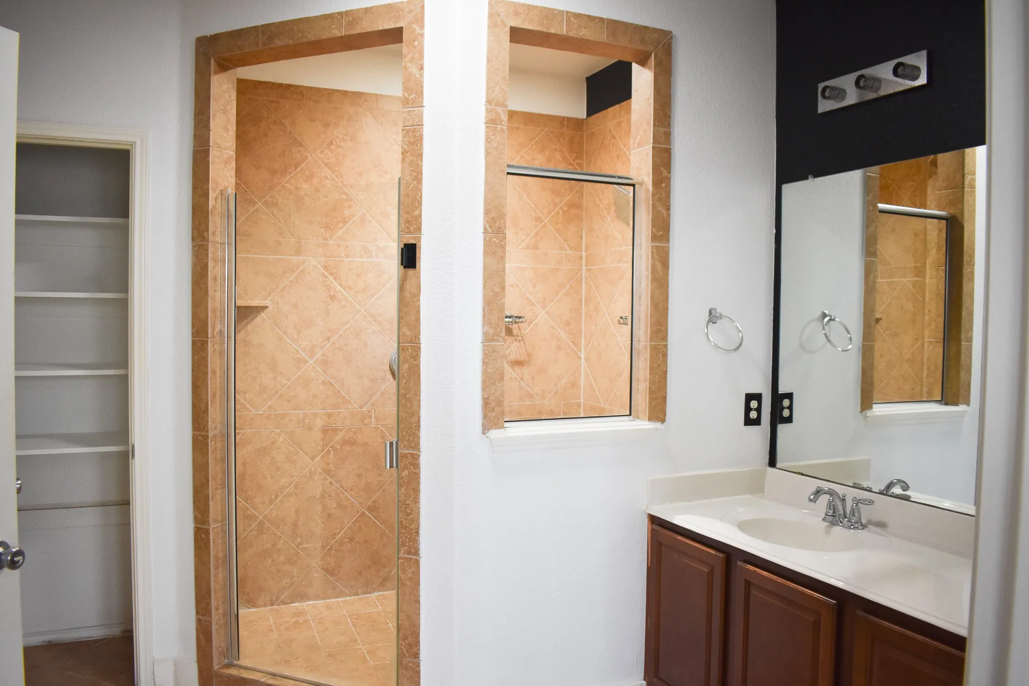 Bathroom featuring a tiled standing shower, a vanity with wood-finish cabinetry, an integrated sink, and a large mirror