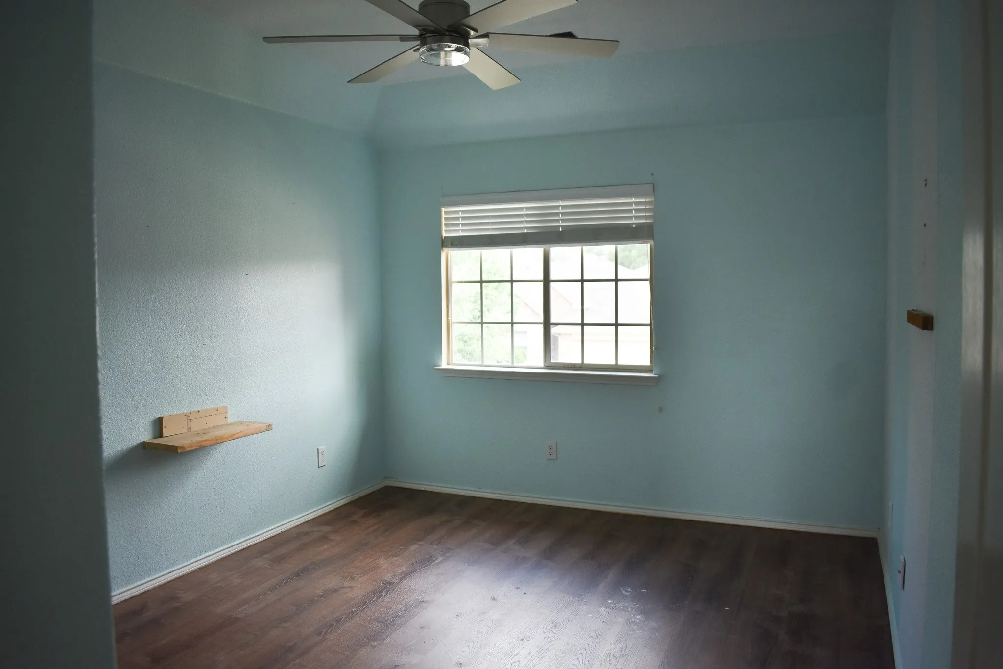 Bright room featuring wood-finish flooring, a window with horizontal blinds, and a ceiling fan with integrated lighting