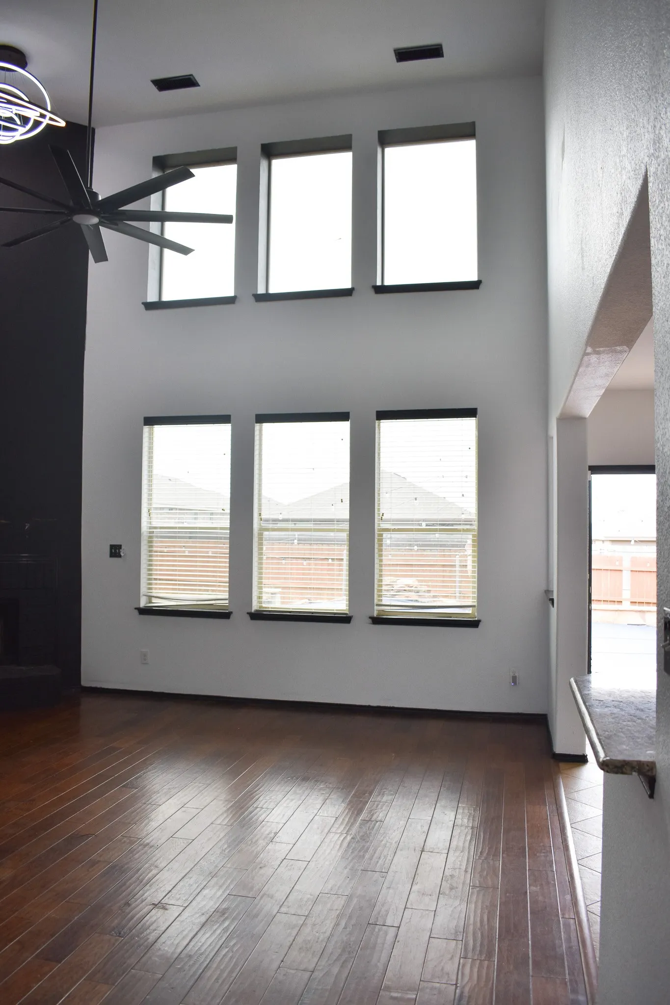 Double-height interior space featuring six vertical windows, dark wood-finish flooring, and a modern ceiling fan with integrated lighting