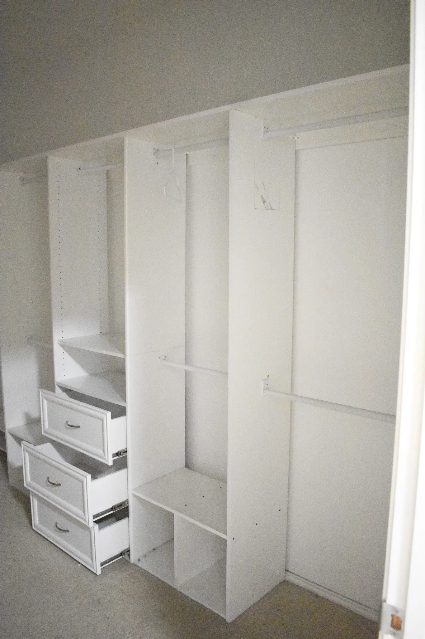 Custom white closet system featuring multiple hanging rods, adjustable shelving, and integrated drawers with silver hardware