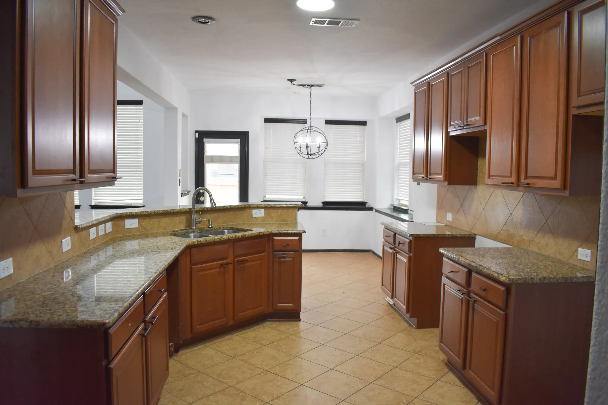 Kitchen featuring abundant wood cabinetry, granite countertops, tile backsplash, stainless steel sink, and tile flooring