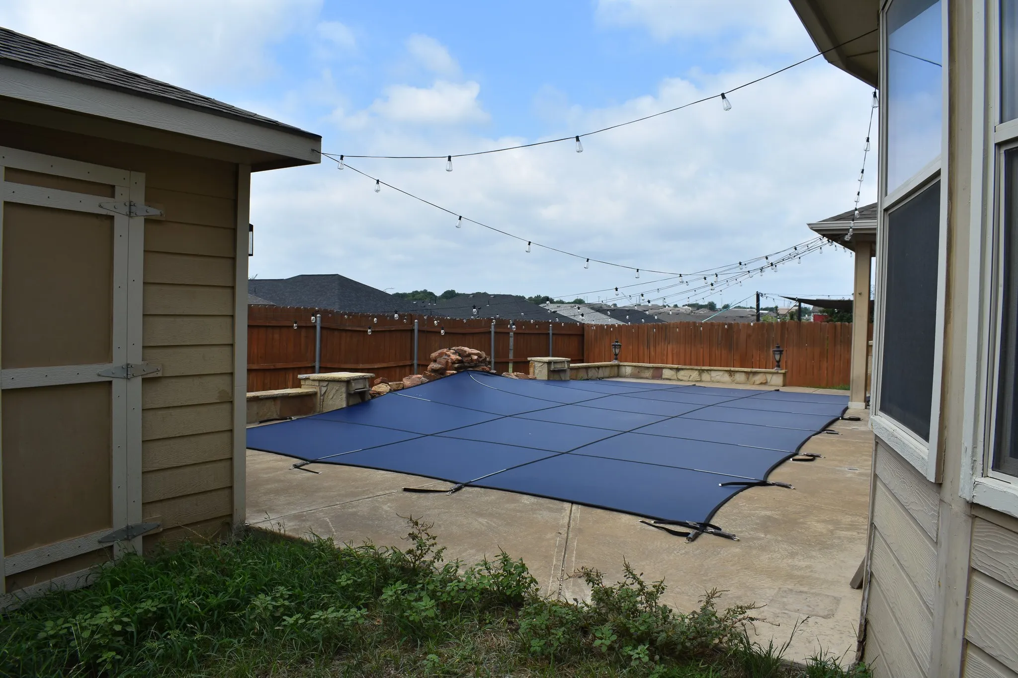 Outdoor swimming pool featuring a dark blue safety cover, concrete surround, and perimeter string lighting