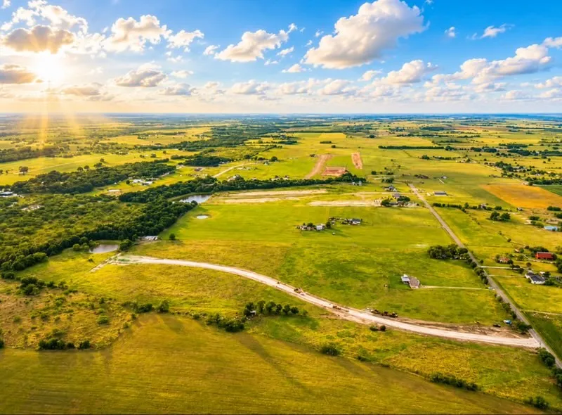 Expansive rural landscape featuring vast green fields and scattered treelines under a bright sky