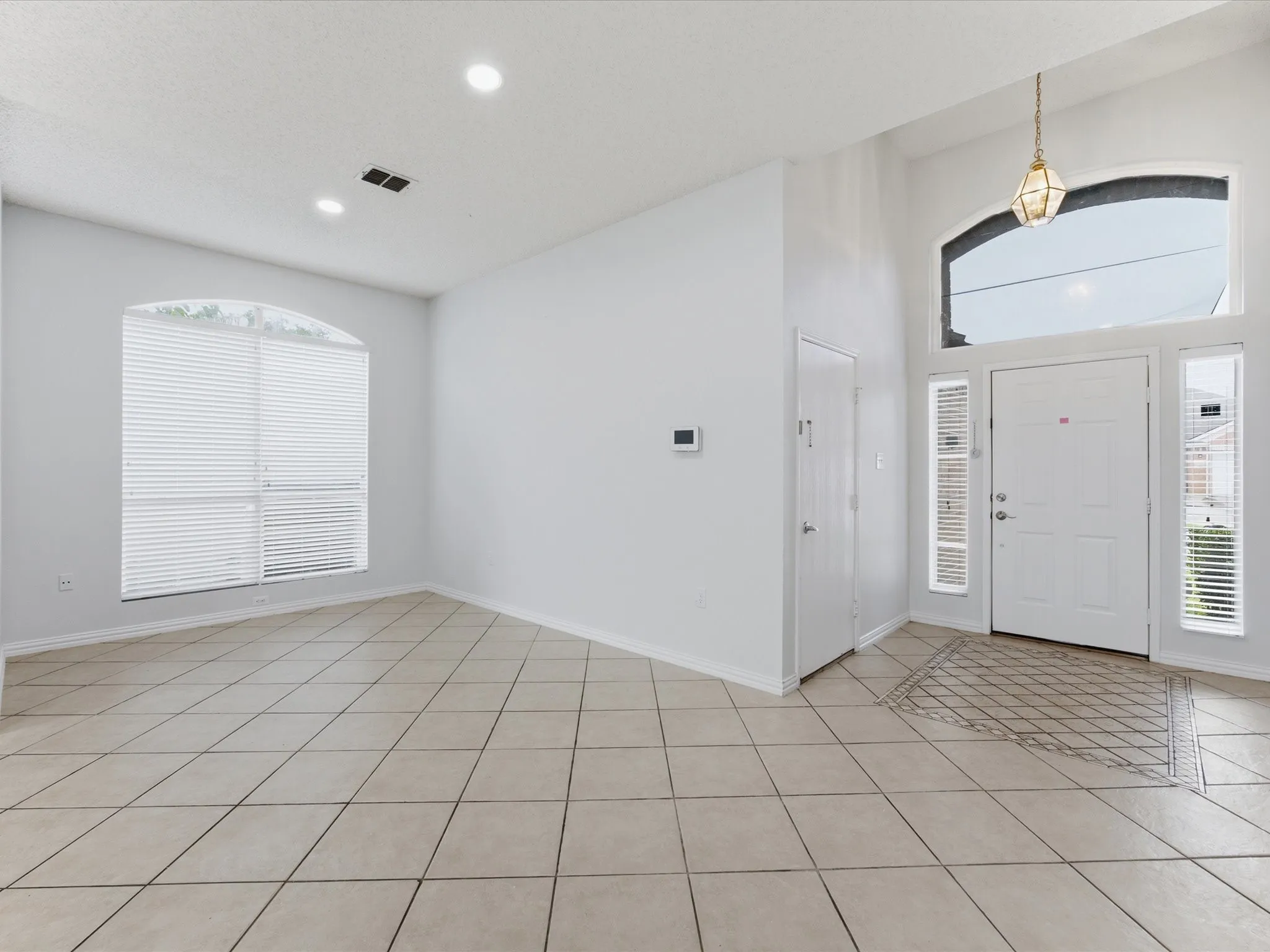 Foyer and living area featuring high ceilings, neutral tile flooring, a paneled front door with side lights, and an arched window with horizontal blinds