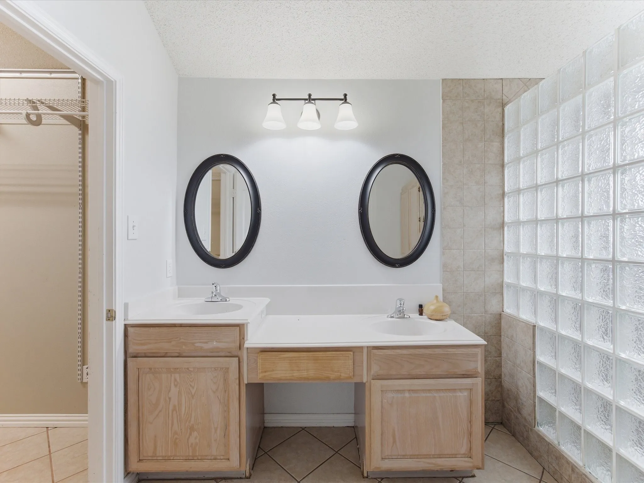 Bathroom featuring a double vanity with white countertops, light wood-finish cabinetry, and oval mirrors