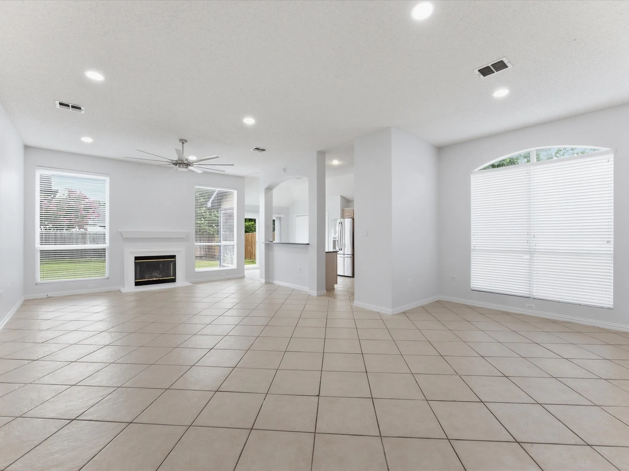Spacious living area featuring neutral tile flooring, a white mantel fireplace, and recessed ceiling lighting