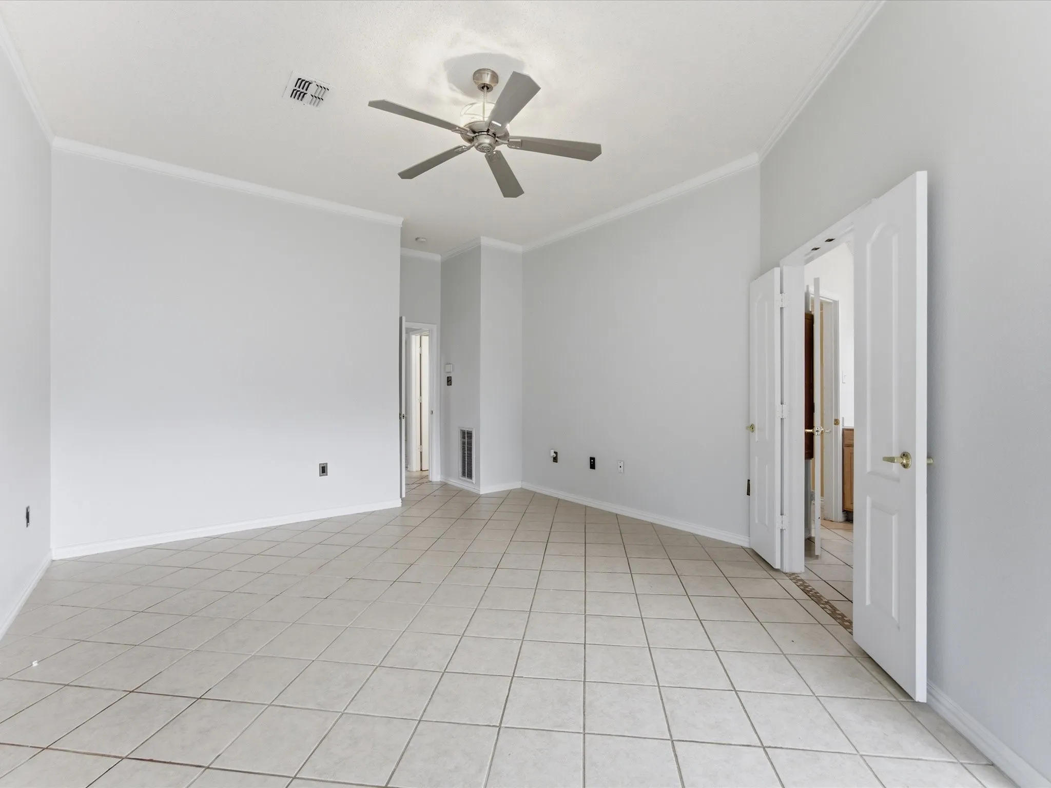 Spacious room with large format tile flooring, crown molding, and a ceiling fan