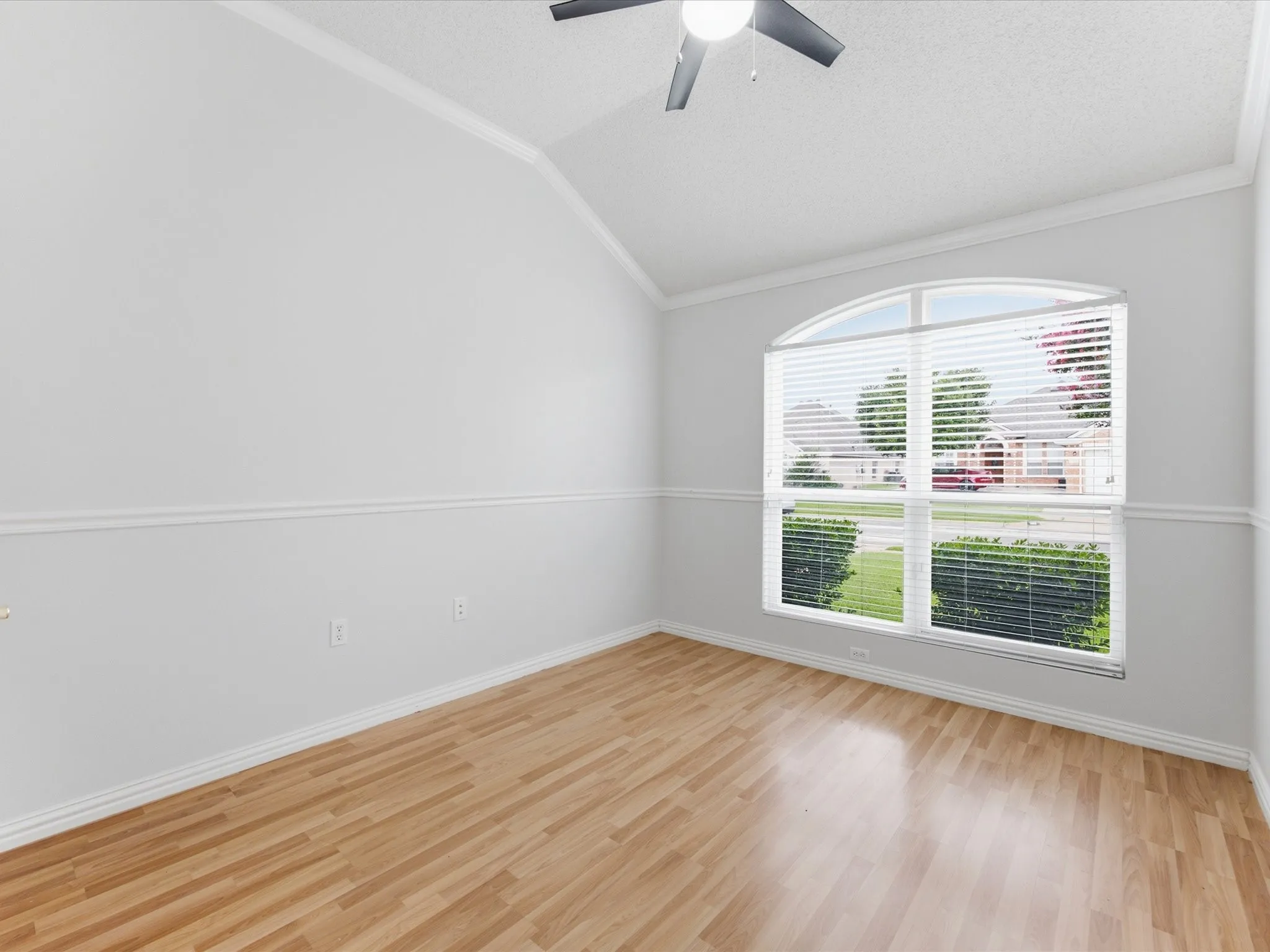 Arched window with blinds, wood-finish flooring, vaulted ceiling, crown molding, and a ceiling fan