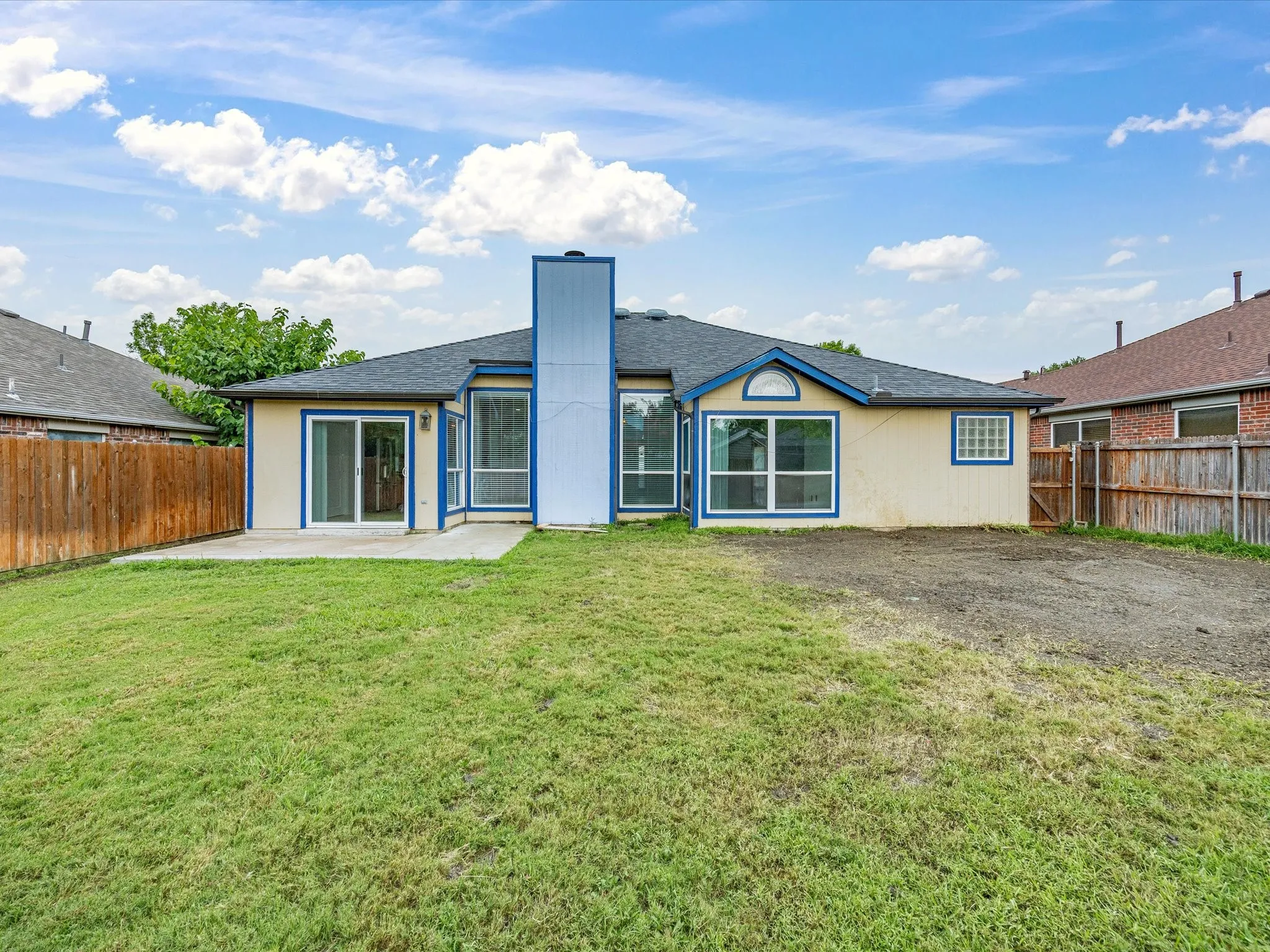 Expansive backyard featuring a concrete patio, sliding glass doors, a blue-trimmed window bay, and a privacy fence