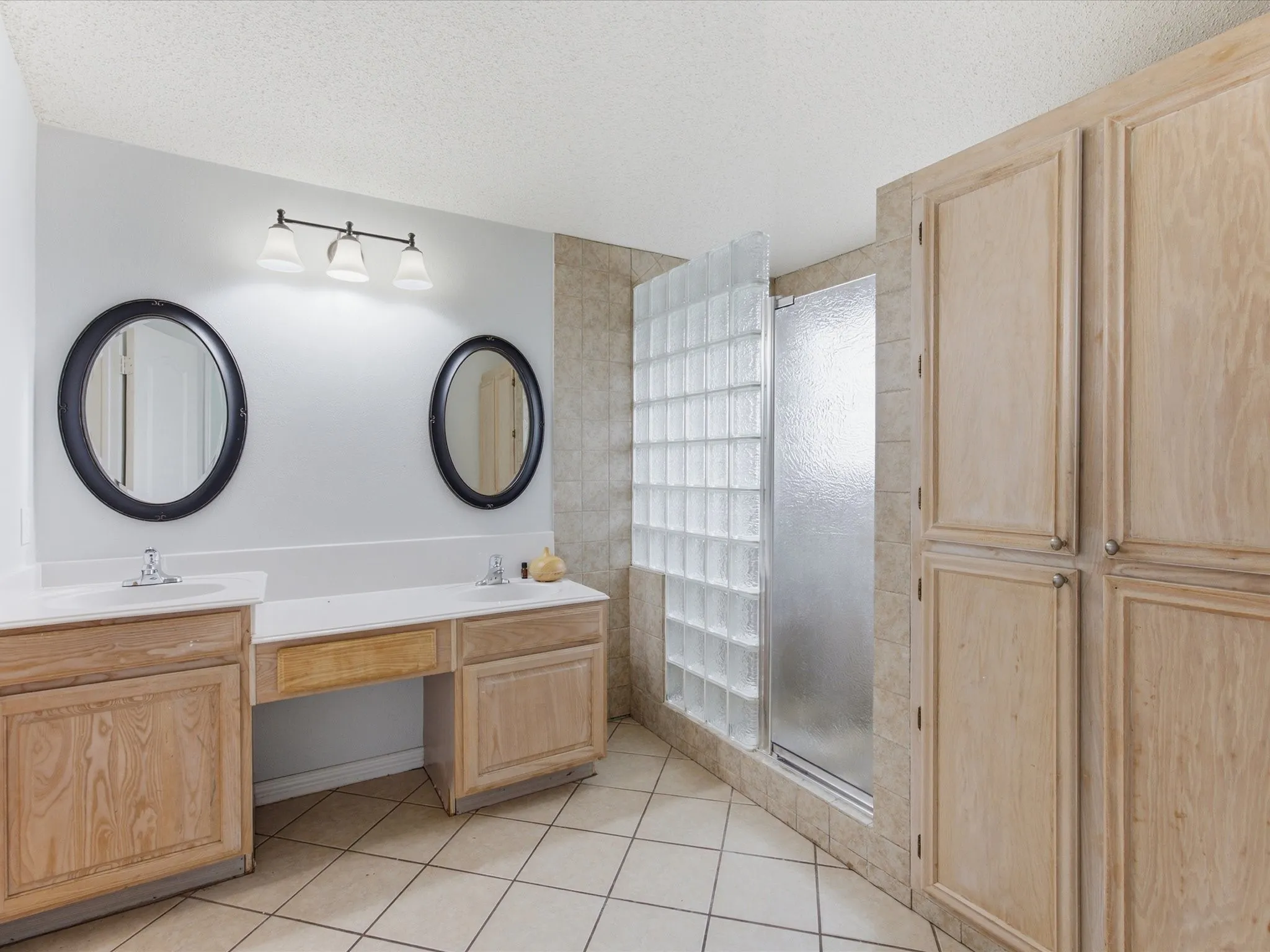 Bathroom featuring a dual vanity with light wood-finish cabinetry, white countertops, and circular mirrors
