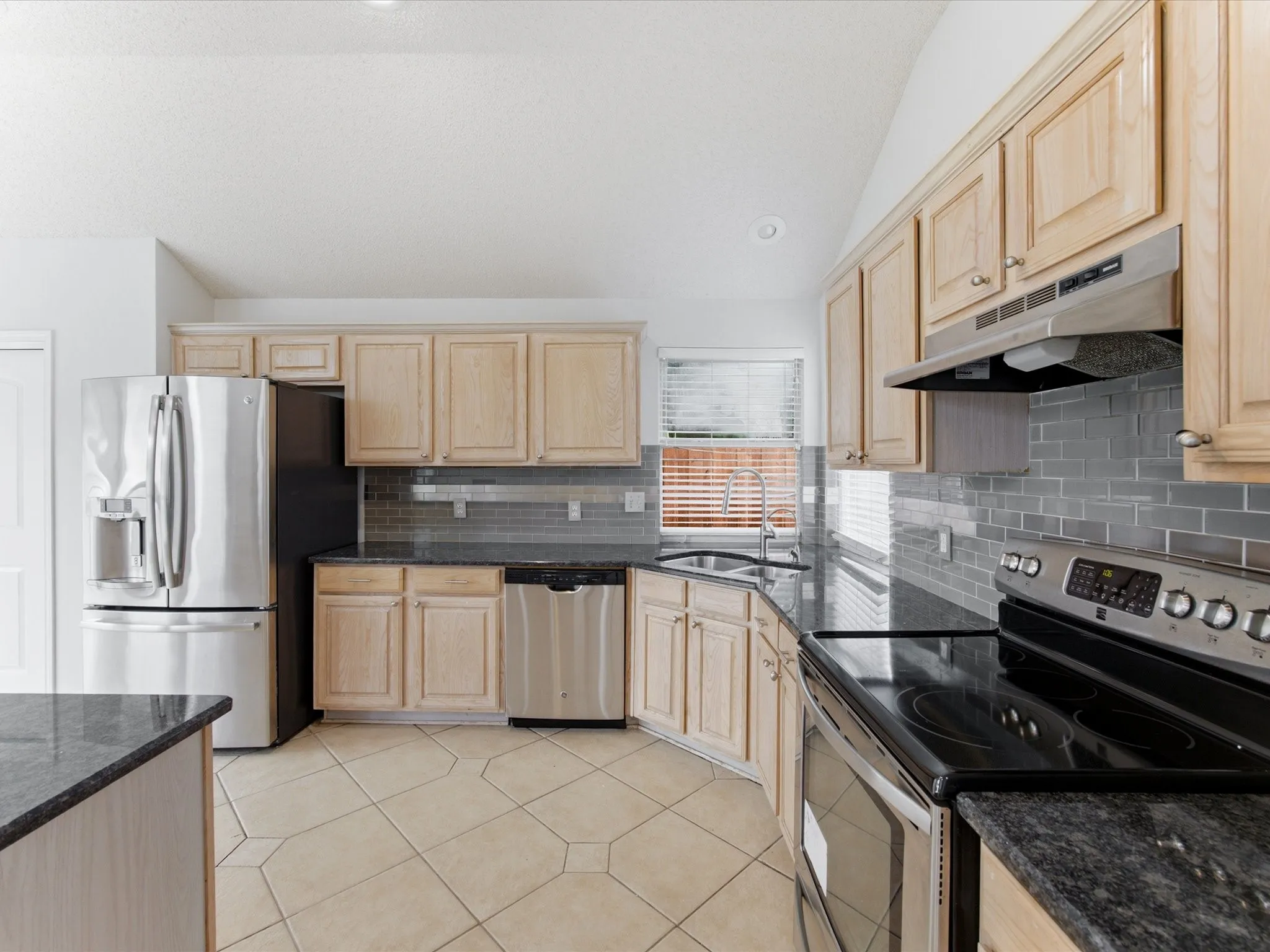 Kitchen featuring wood cabinetry, dark granite countertops, stainless steel appliances, a subway tile backsplash, and ceramic tile flooring