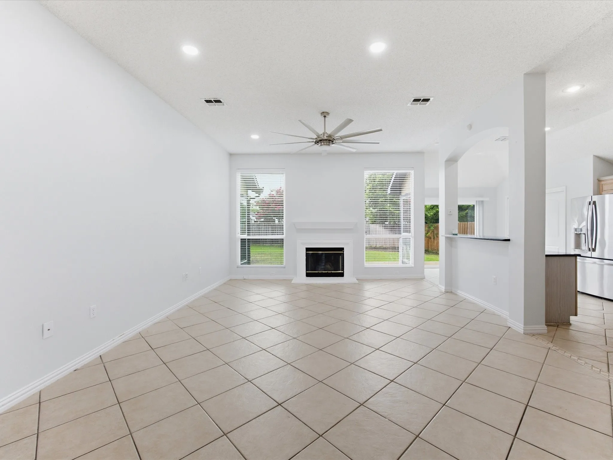 Spacious living area featuring large format tile flooring, a built-in fireplace with white mantel, a ceiling fan, and recessed lighting