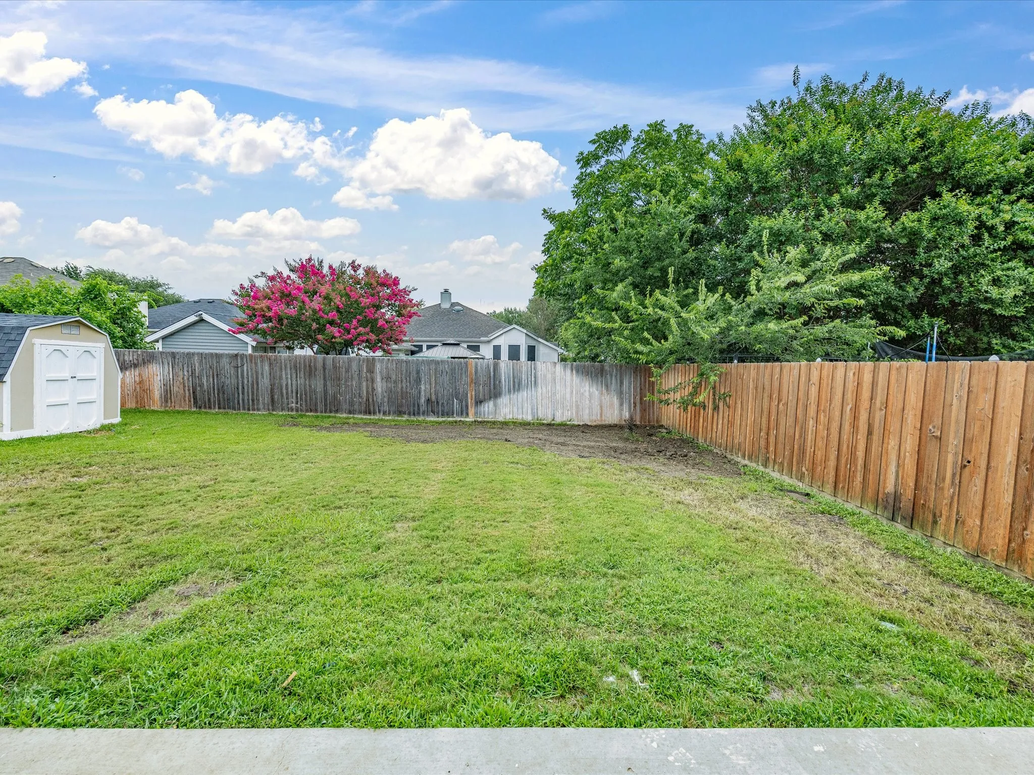 Expansive grassy backyard featuring a wood fence, a storage shed, and mature trees