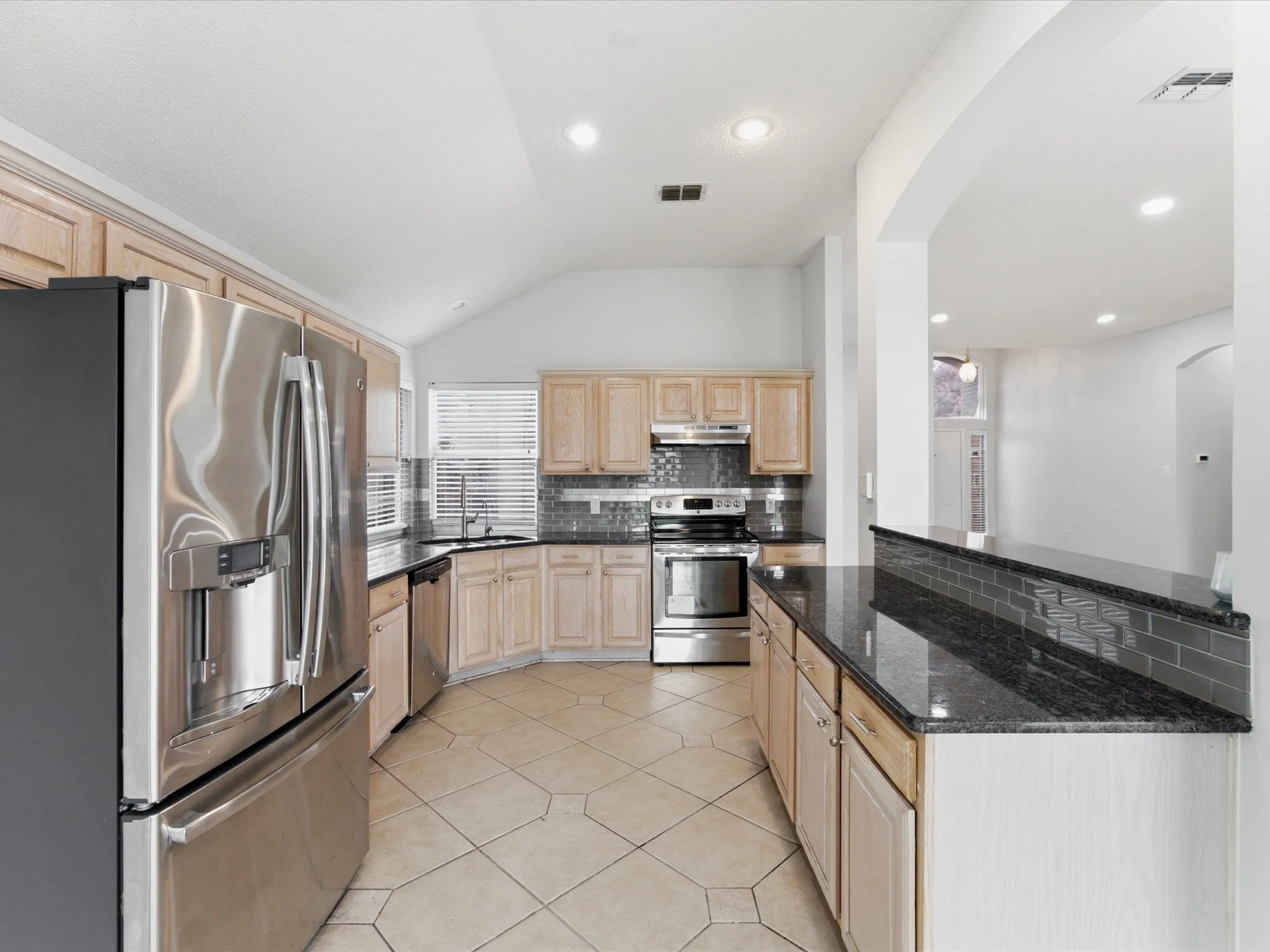 Kitchen featuring stainless steel appliances, light wood-finish cabinetry, dark stone countertops, and tile flooring