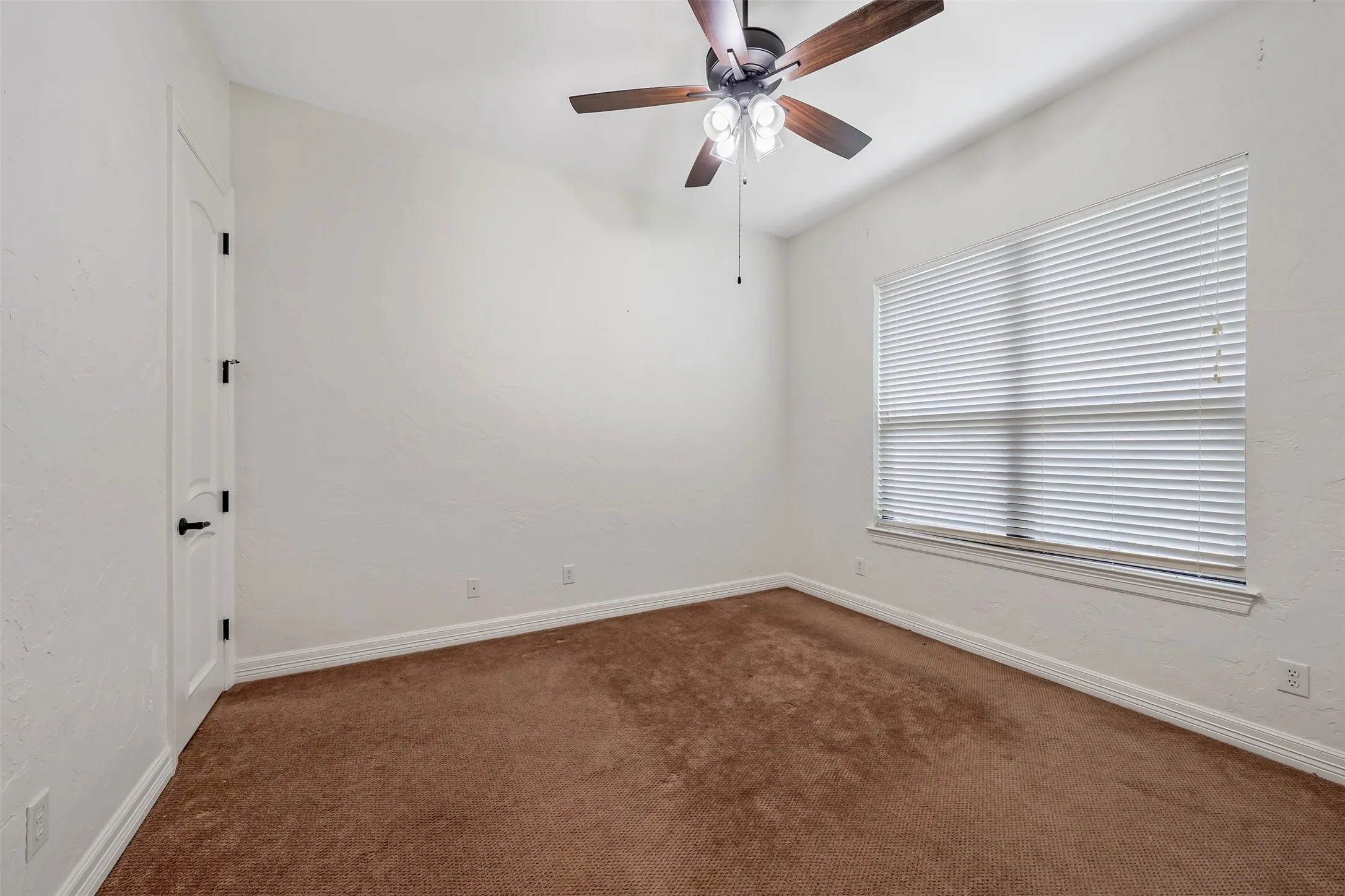 Interior room featuring neutral wall paint, brown carpeting, a window with horizontal blinds, and a ceiling fan with integrated lighting