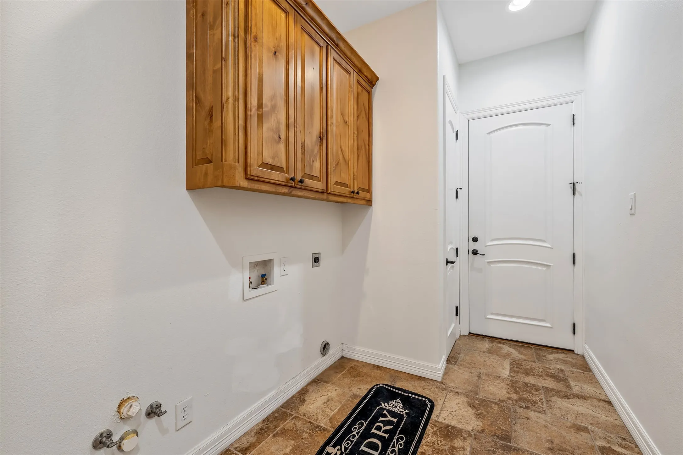 Laundry area with warm wood cabinetry, neutral wall paint, and patterned tile flooring
