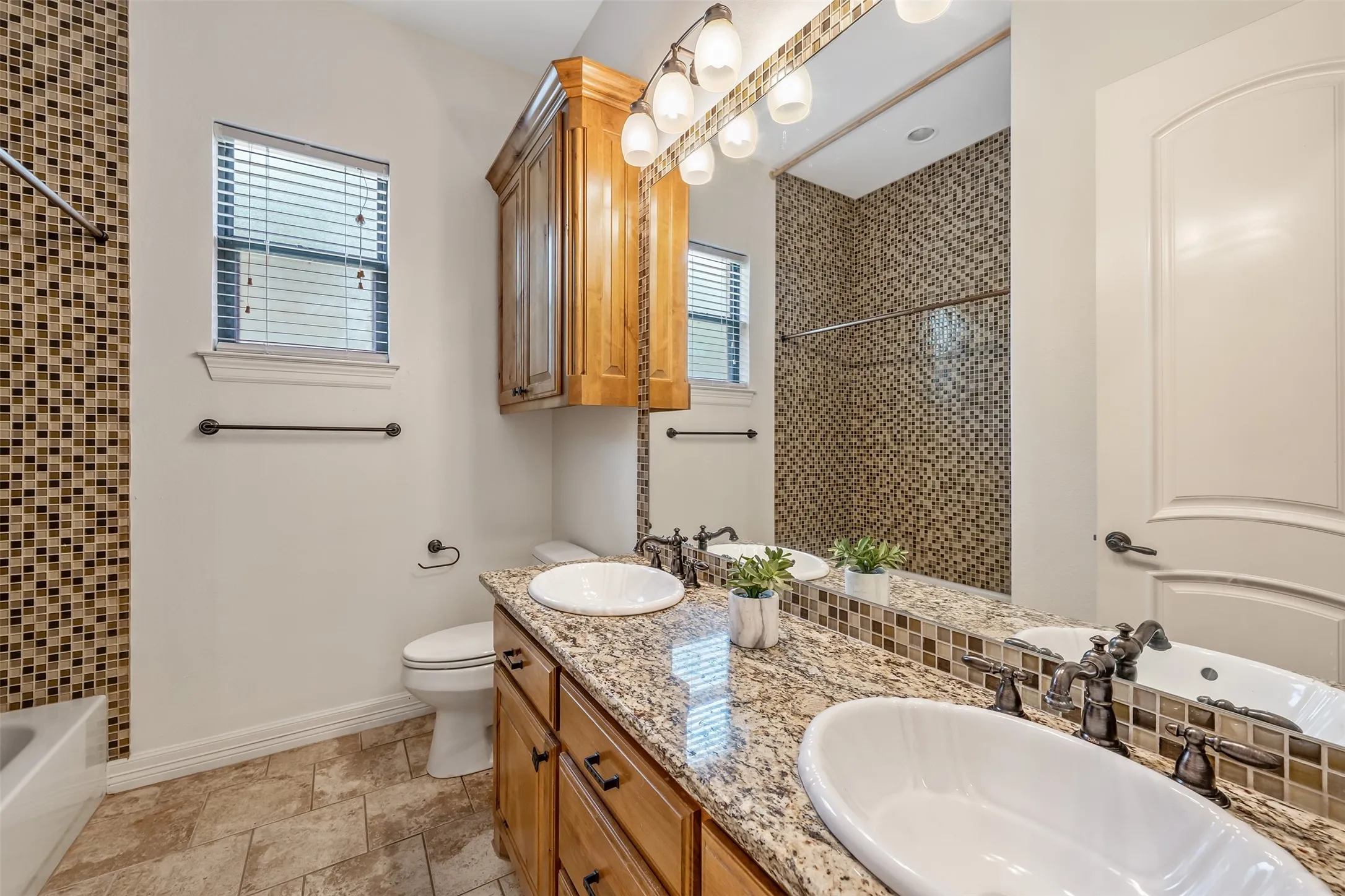 Bathroom featuring a dual vanity with granite-finish countertop, wood-finish cabinetry, and vessel sinks