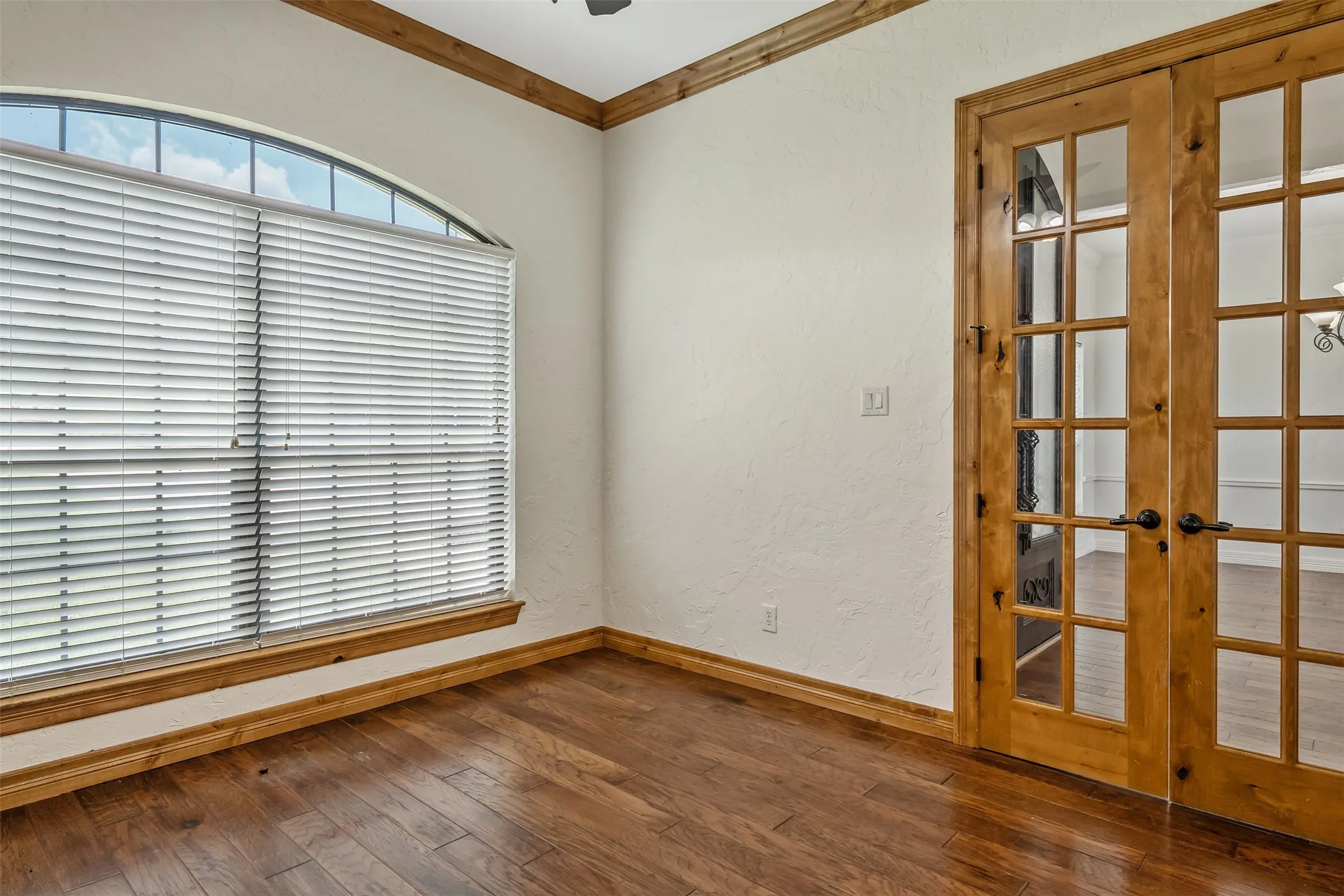 Arch-top window with blinds, wood-finish flooring, and natural wood French doors