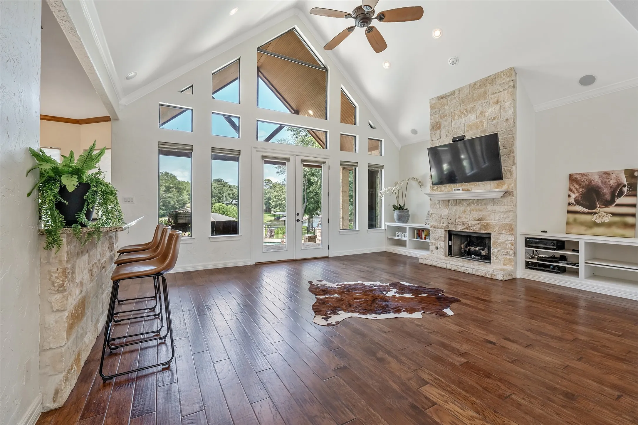 Living area featuring an expansive vaulted ceiling with exposed beams, wood-finish flooring, a stone-clad fireplace, and built-in shelving