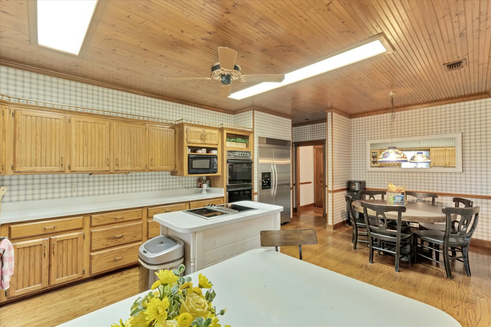 Spacious kitchen featuring light wood cabinetry, a central island with cooktop, stainless steel appliances, sub-zero refrigerator and wood-finish flooring