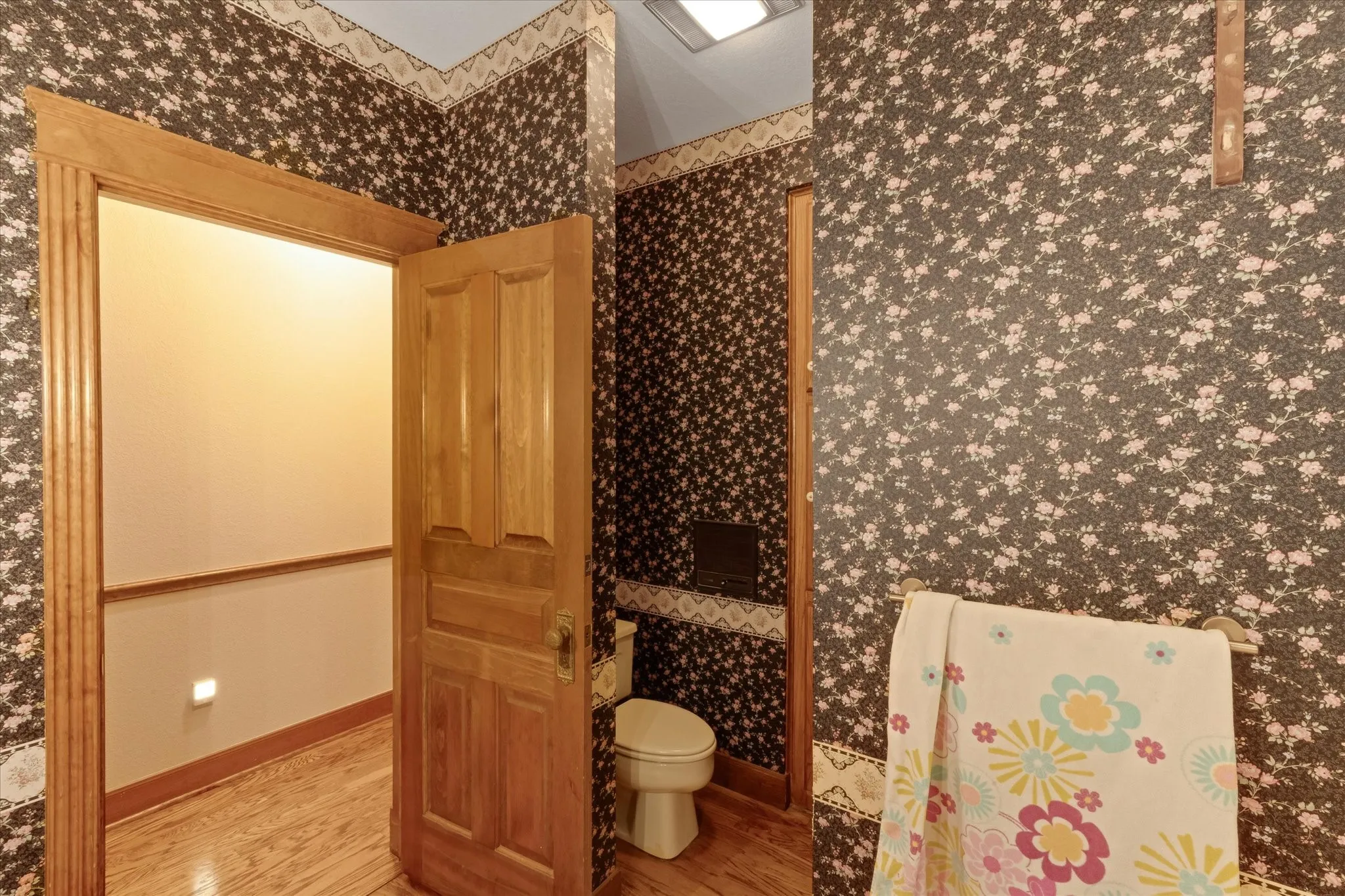 Interior space featuring wood-finish flooring, a traditional paneled wood door with fluted trim, and floral wallpaper with a complementary border