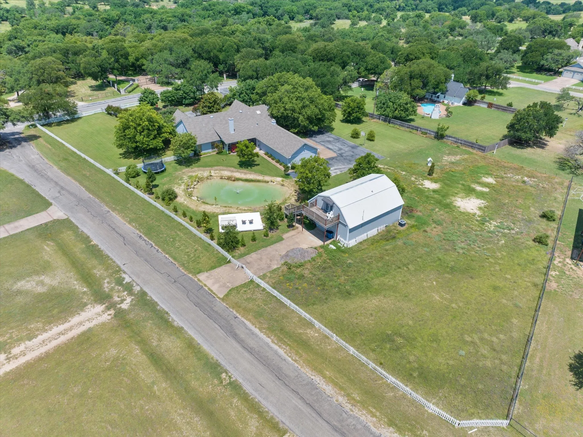 Expansive property featuring a main residence, secondary detached structure with a balcony, private pond, and perimeter fencing