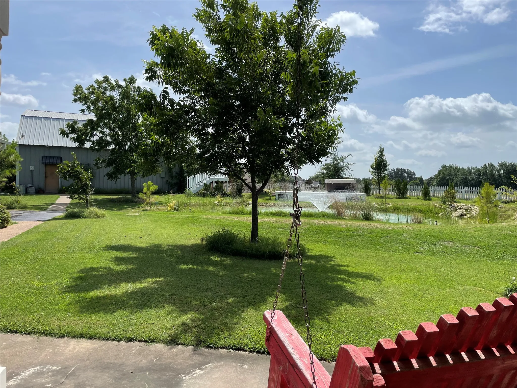 Expansive outdoor space featuring a manicured lawn, established trees, and a decorative pond with a central fountain