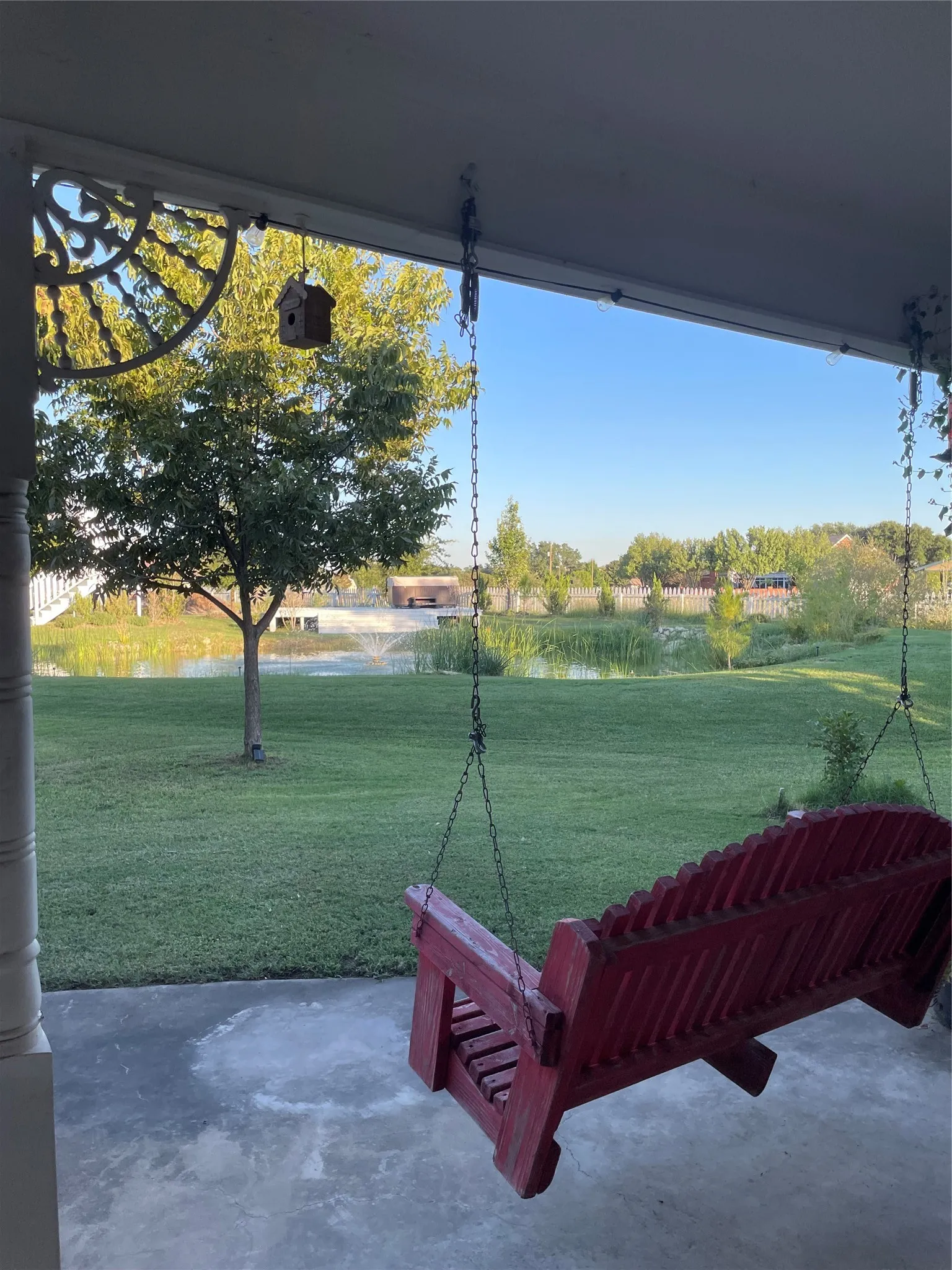 Covered porch with decorative white spindle details, overlooking a manicured lawn and serene pond