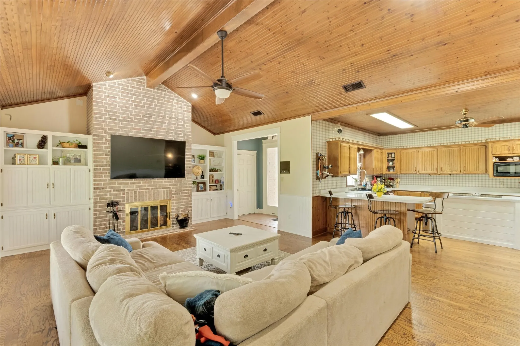 Spacious living area featuring a vaulted wood-plank ceiling, brick fireplace with a gold-tone screen, and built-in white cabinetry