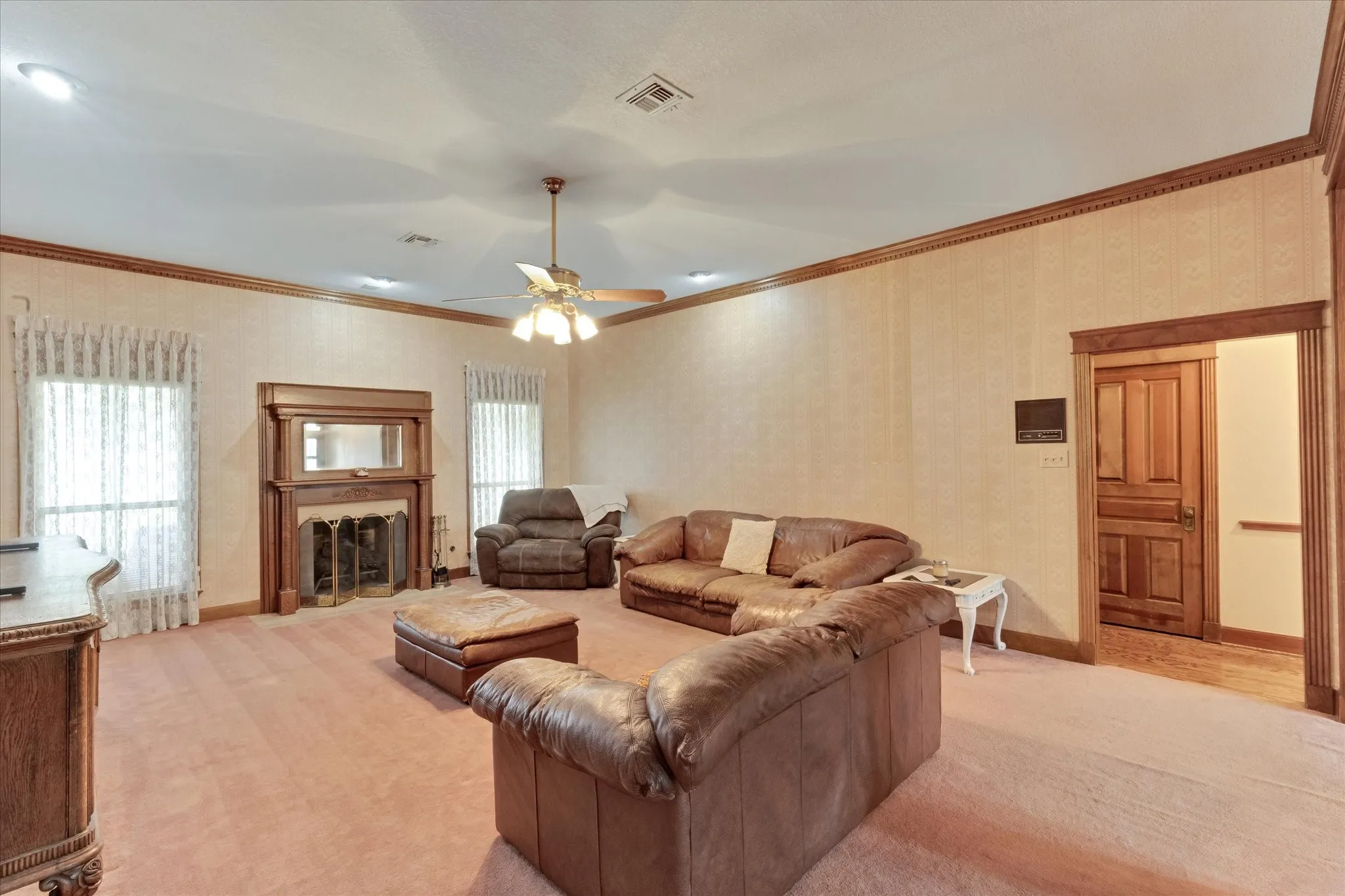 Spacious living area featuring a wood-mantled fireplace with an integrated mirror, two windows, and a ceiling fan