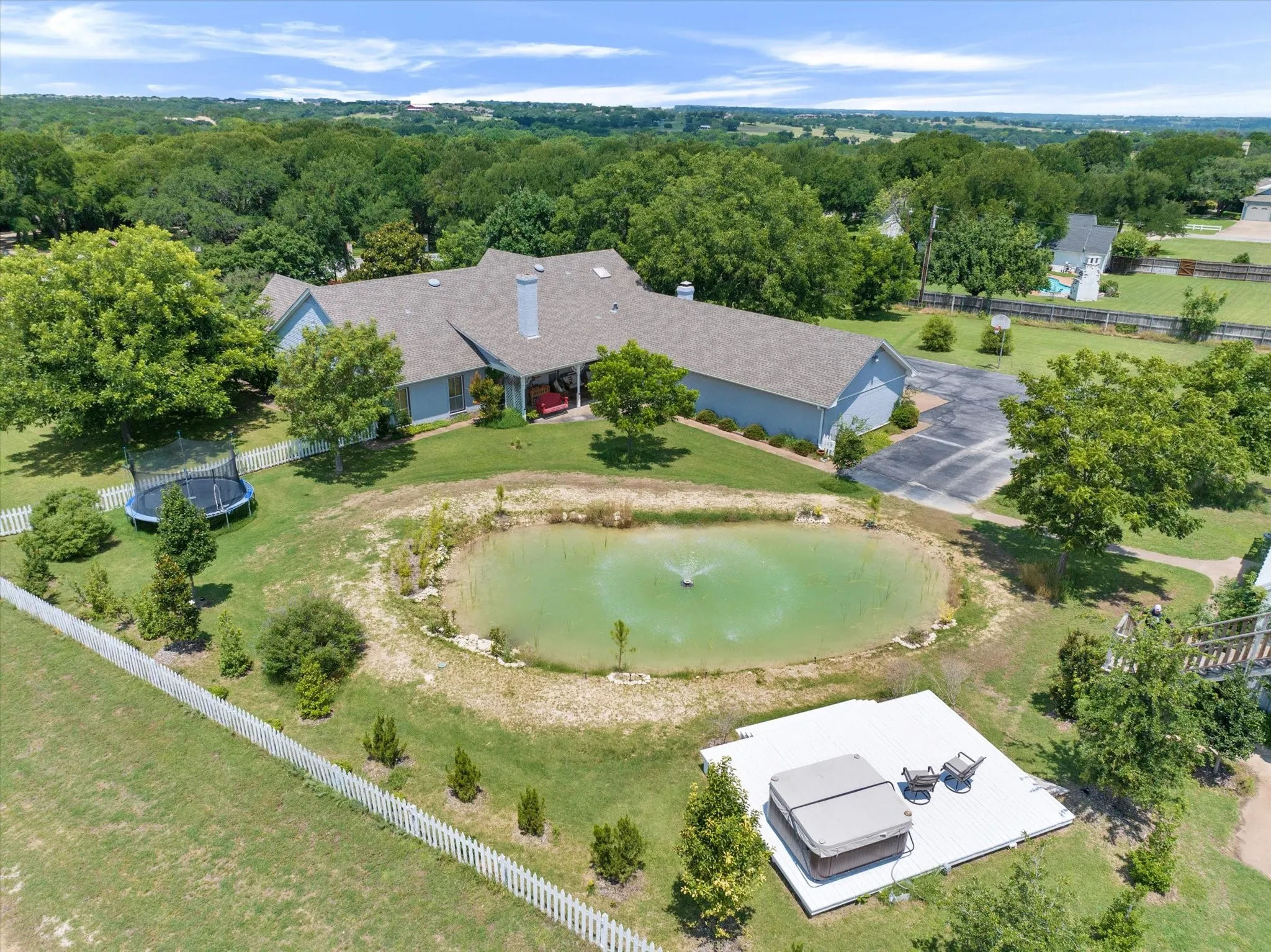 Expansive property featuring a large pond with a fountain, a paved driveway, and a white picket fence