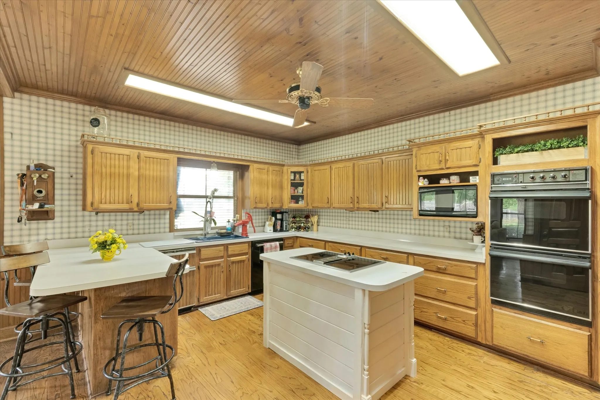 Kitchen featuring wood-finish flooring, beadboard ceiling, double ovens, and light wood cabinetry