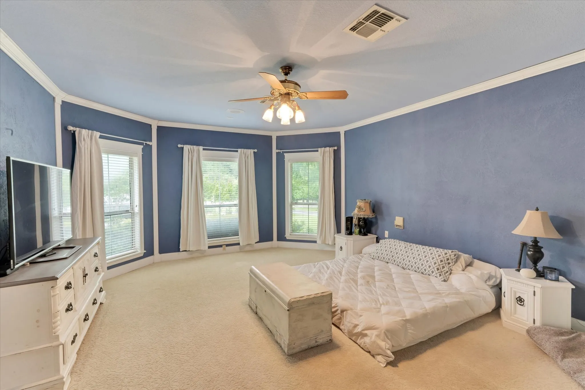 Spacious room featuring multiple windows, crown molding, a ceiling fan with integrated lighting, and neutral-toned carpeting. Primary bedroom