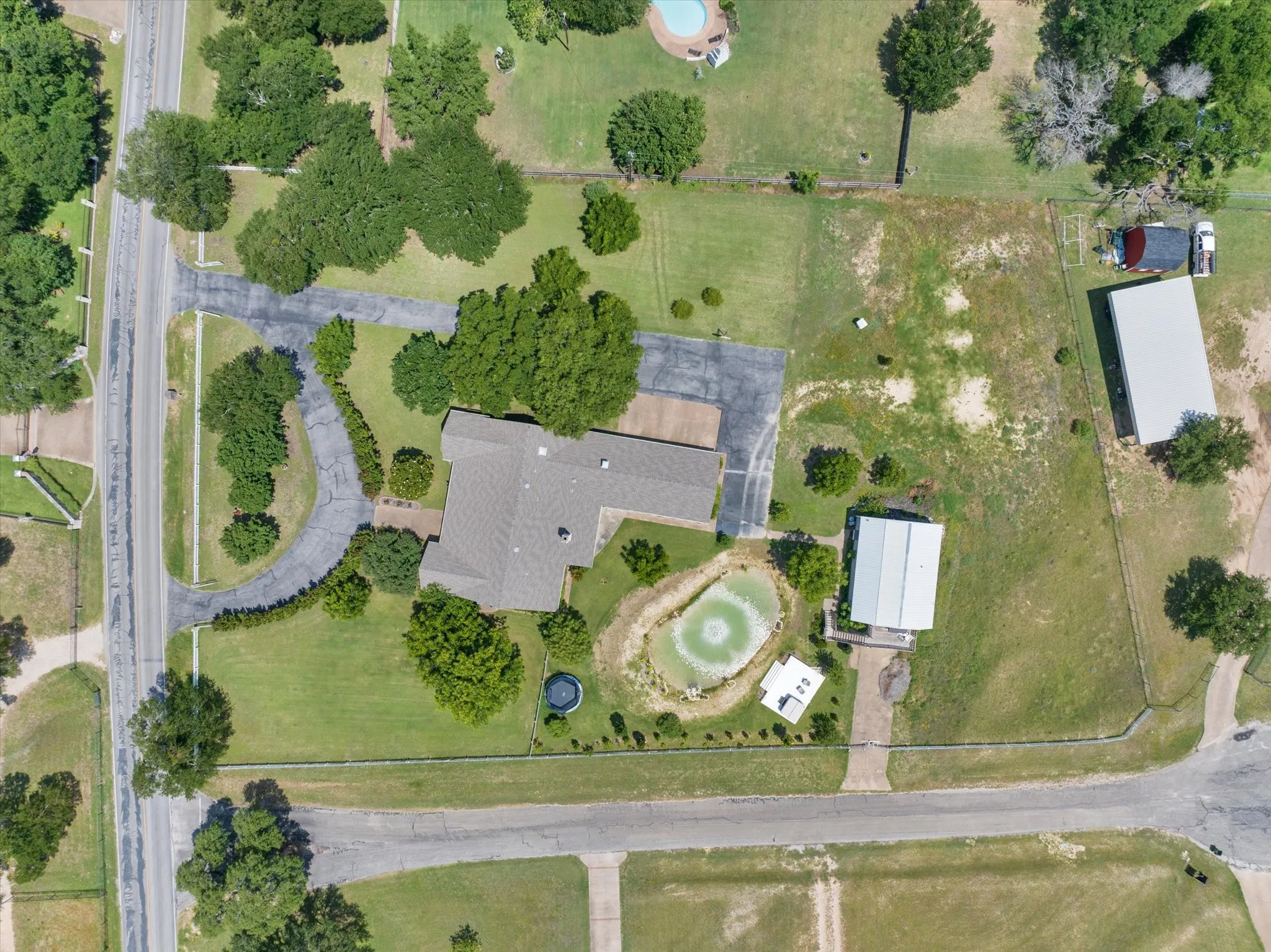 Expansive property featuring a central residence with a gabled roofline, a large paved driveway, and mature landscaping