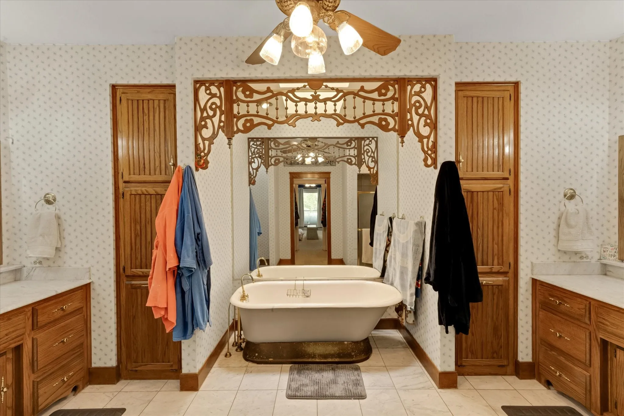 Freestanding bathtub centered between two wood-finish vanity cabinets with stone countertops, Sky light in primary bathroom