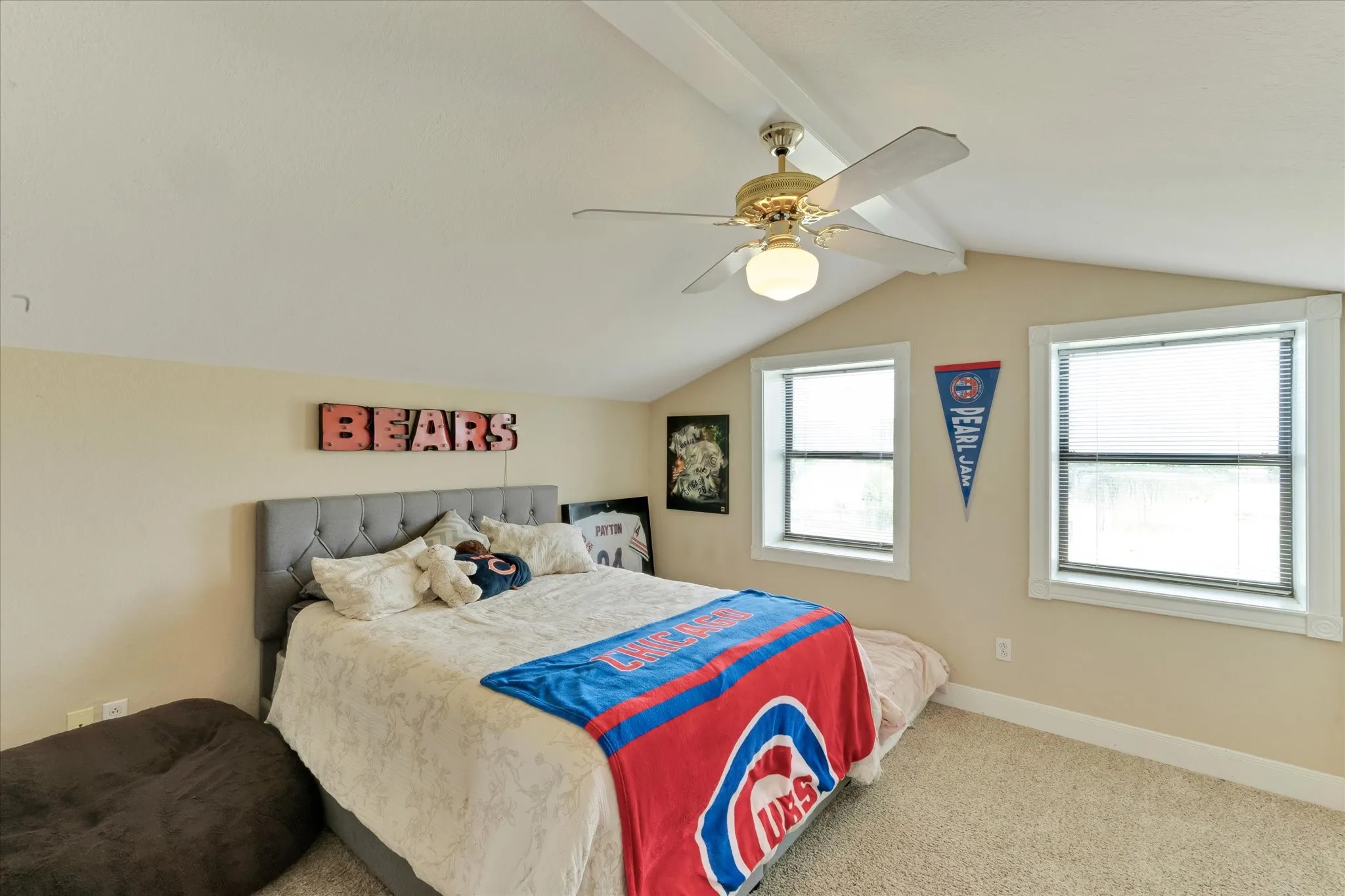 Carpeted room featuring a sloped ceiling with exposed beam, two windows, and a ceiling fan with integrated lighting. Guest house bedroom