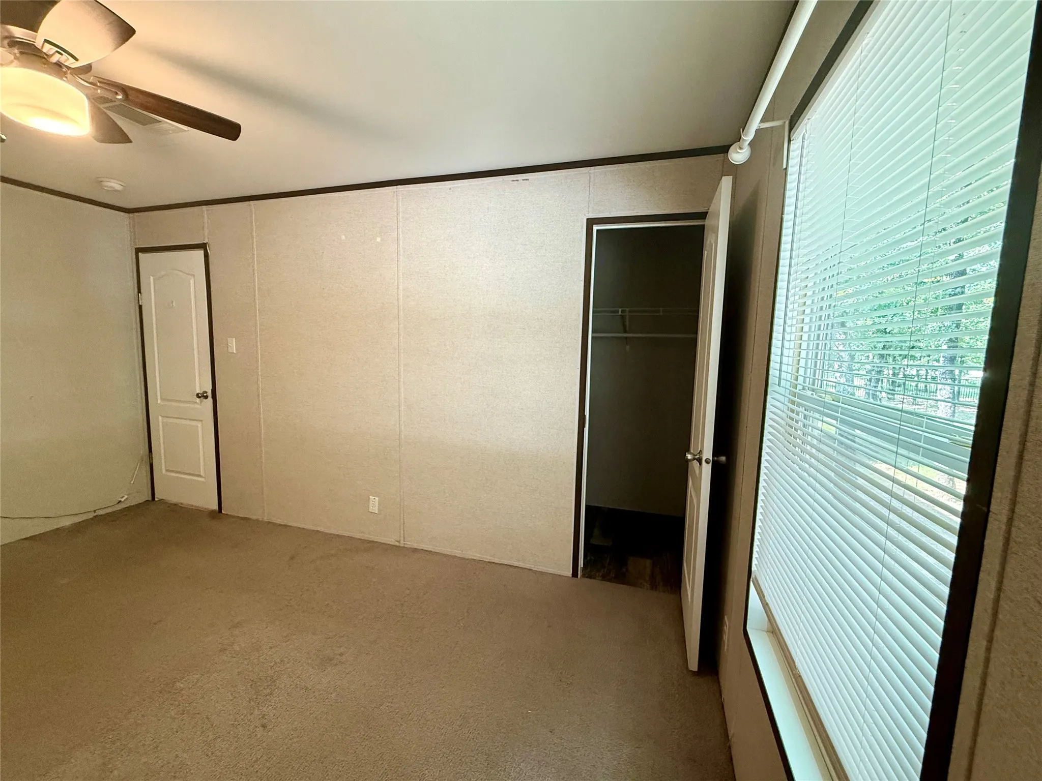 Carpeted room featuring a ceiling fan with integrated lighting, a panel door, and a window with blinds