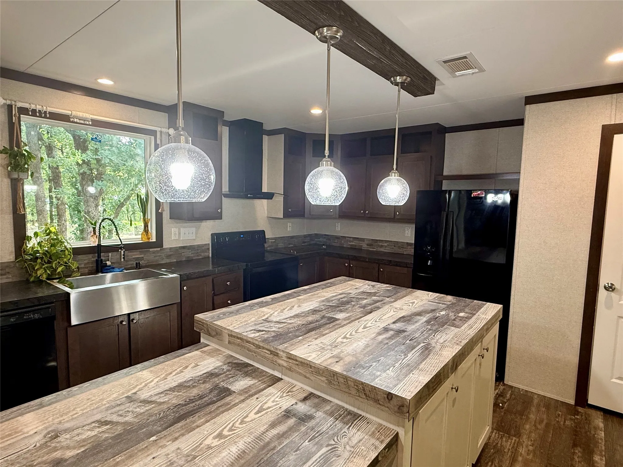Kitchen featuring a multi-level island with wood-finish countertop, stainless steel farmhouse sink, pendant lighting, dark wood cabinetry, and black appliances
