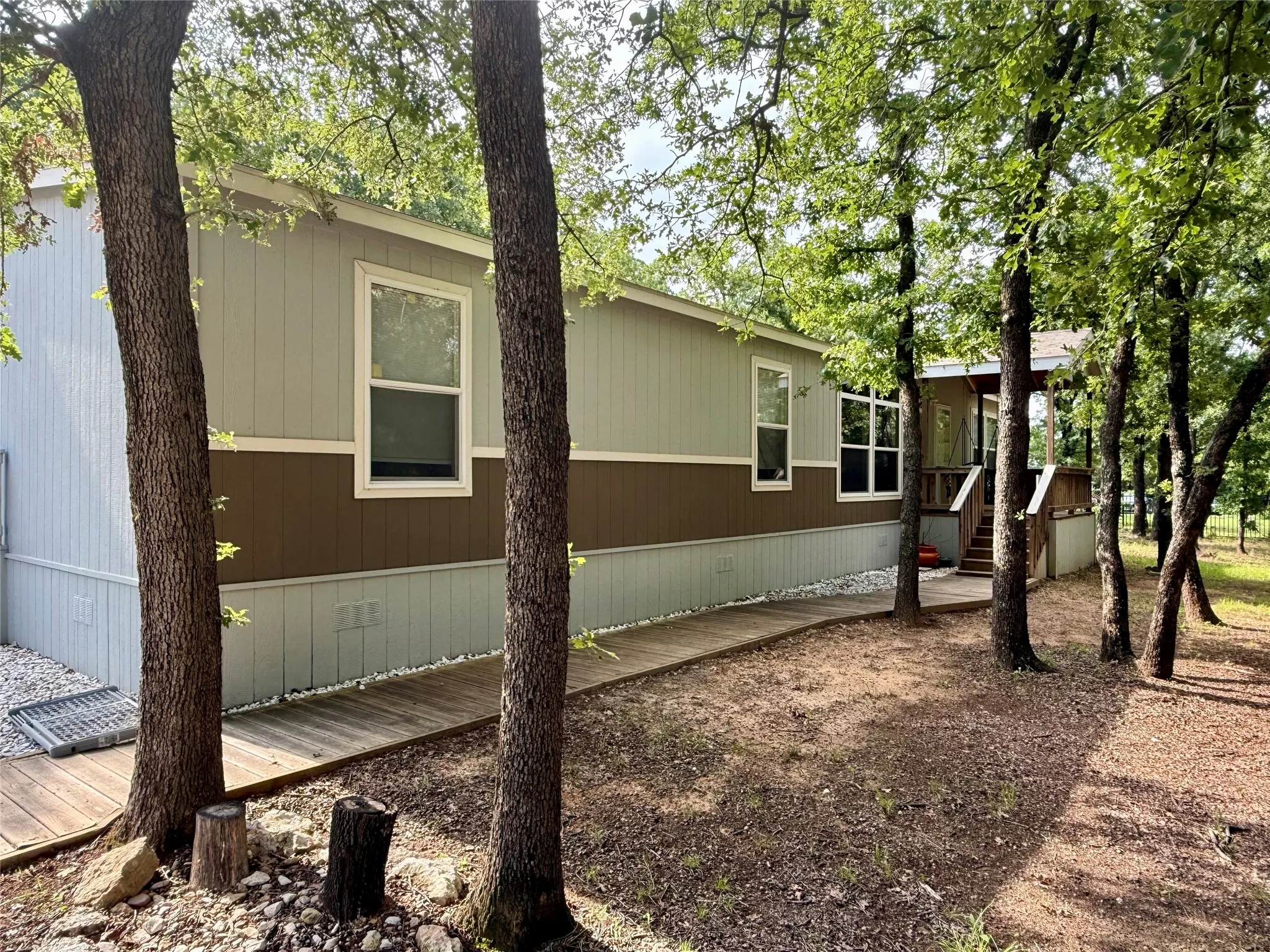 Exterior siding featuring a multi-tone panel design, white-framed windows, a wooden walkway, and mature trees