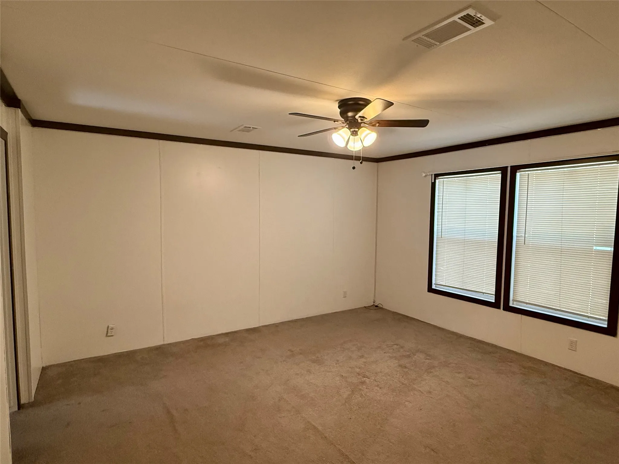 Spacious room featuring carpet flooring, two windows with blinds, a ceiling fan with integrated lighting, and dark trim accents