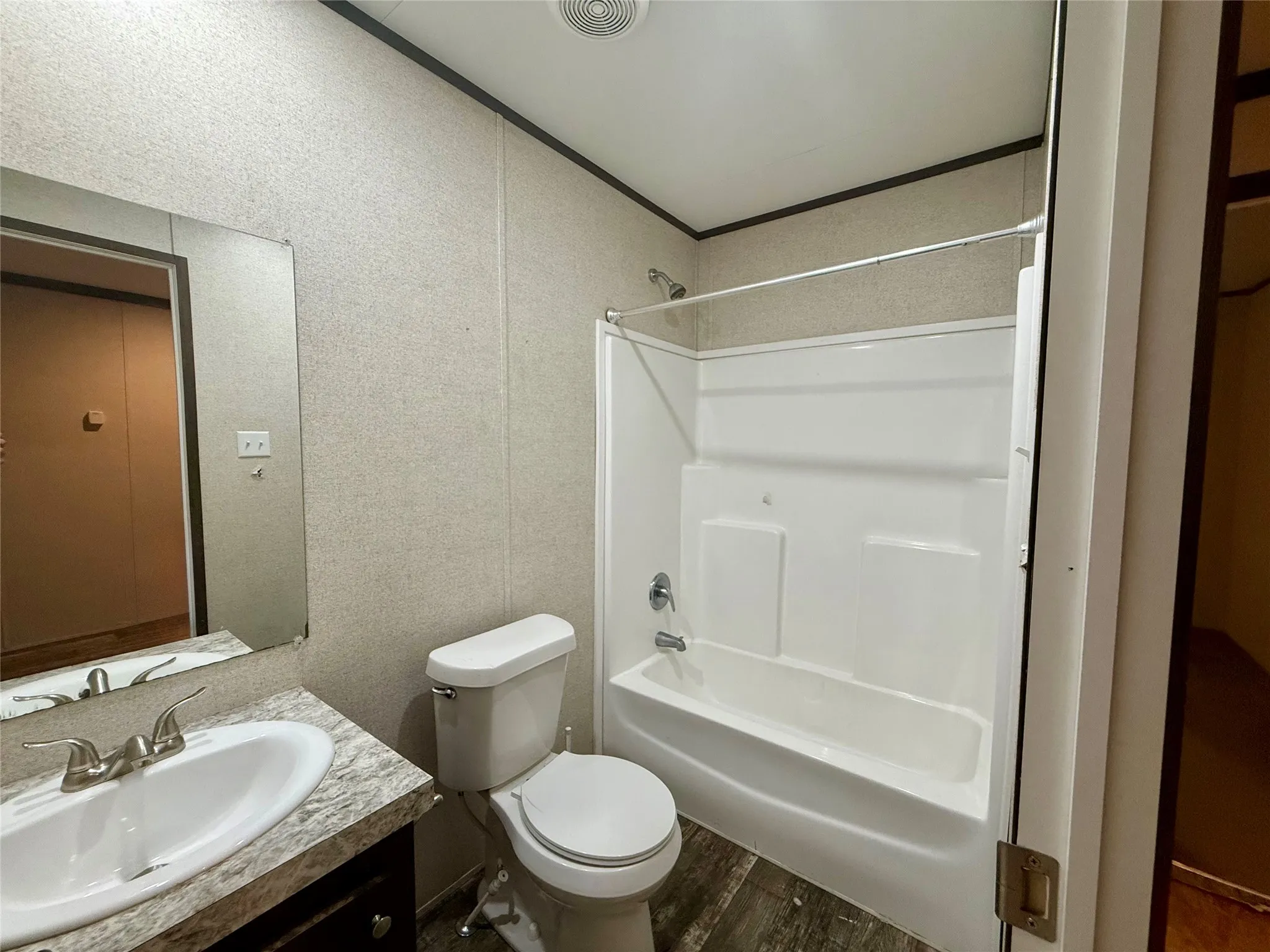 Full bathroom featuring a white combination shower and tub with chrome fixtures, a single vanity with an integrated sink and wood-finish cabinetry, a commode, and wood-finish flooring