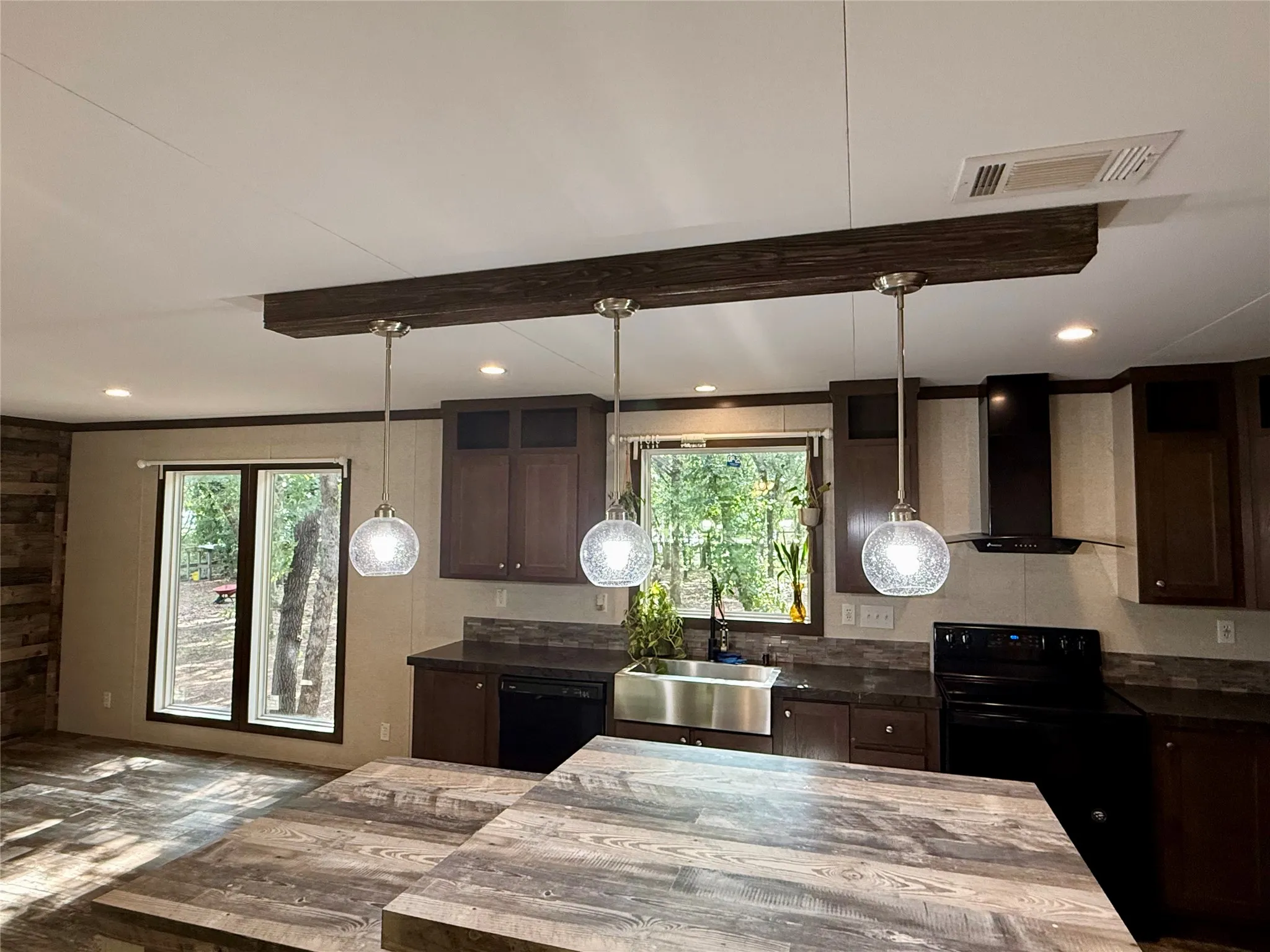 Open concept kitchen and dining area featuring wood-finish flooring, a kitchen island with pendant lighting, dark wood cabinetry, and a farmhouse sink