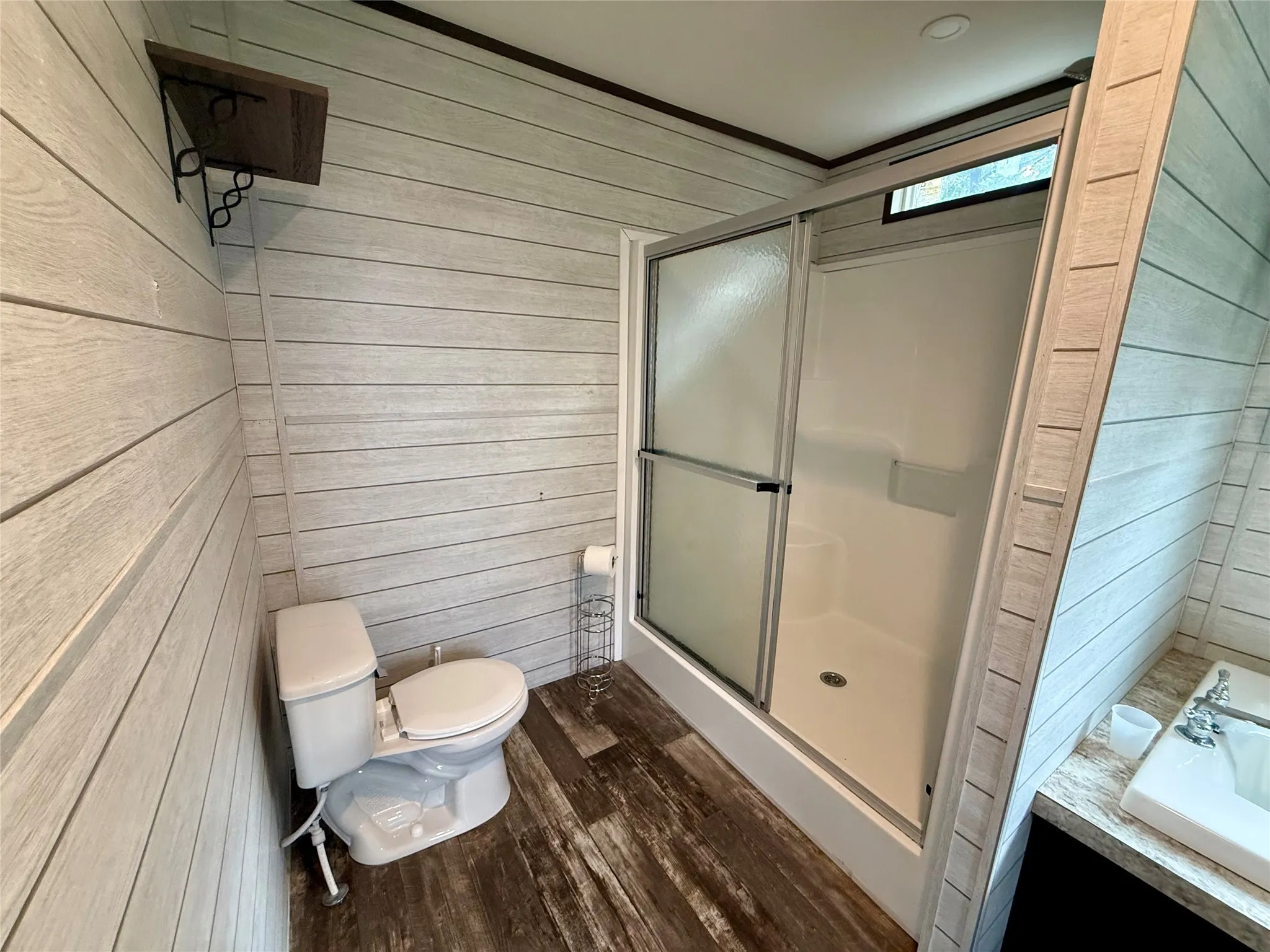 Bathroom featuring a shower with sliding glass doors, white toilet, and wood-finish flooring