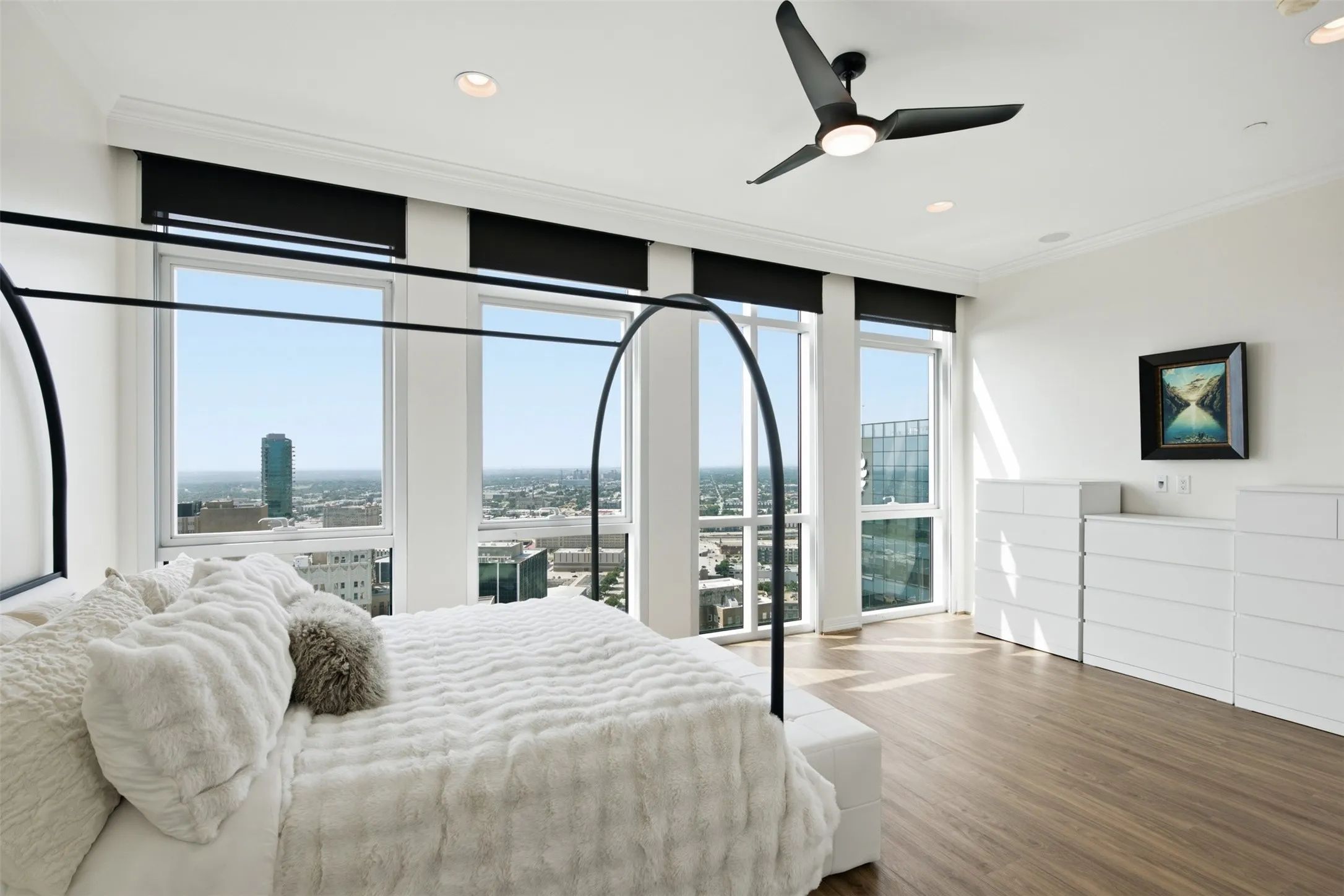 Primary Bedroom offers Floor-to-ceiling windows with electric roller shades including black out shades, wood-finish flooring, recessed lighting, and a contemporary ceiling fan