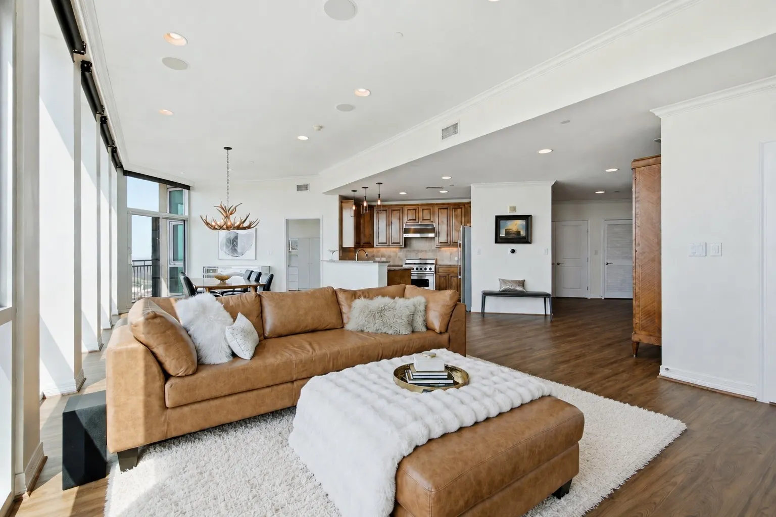 Open-concept living space featuring luxury vinyl plank  wood-finish flooring, recessed lighting, crown molding, and abundant natural light from floor-to-ceiling windows