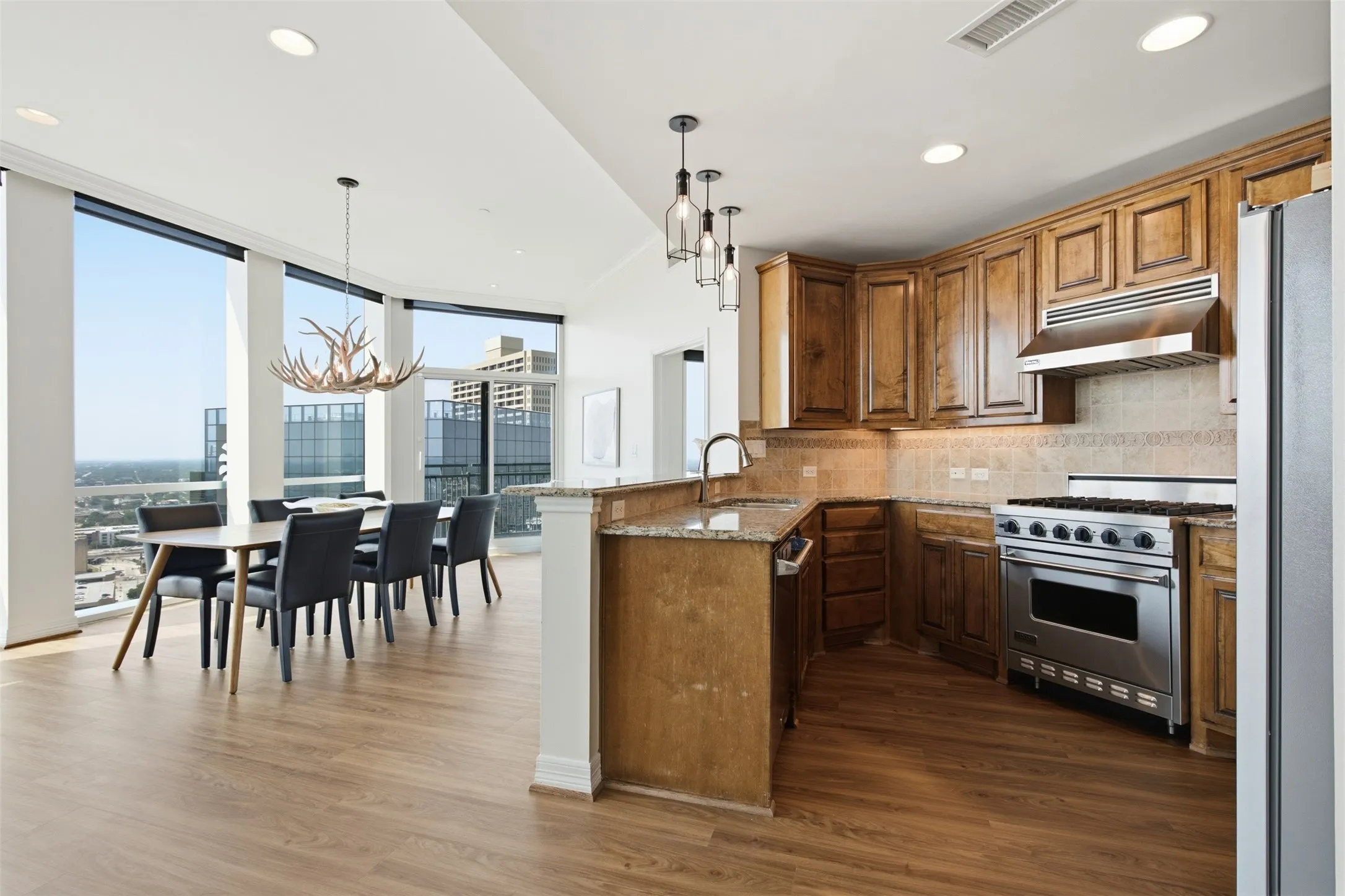Open-concept living space featuring wood-finish flooring, a kitchen with wood cabinetry and stainless steel Viking appliances, and a dining area with floor-to-ceiling windows