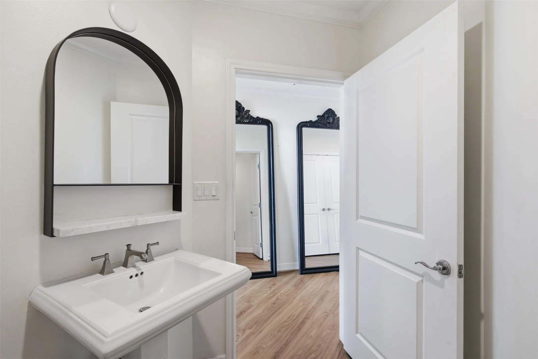 Guest Half Bath off the entry foyer features Pedestal sink with brushed nickel faucet, arched black-framed mirror, and marble-look shelf